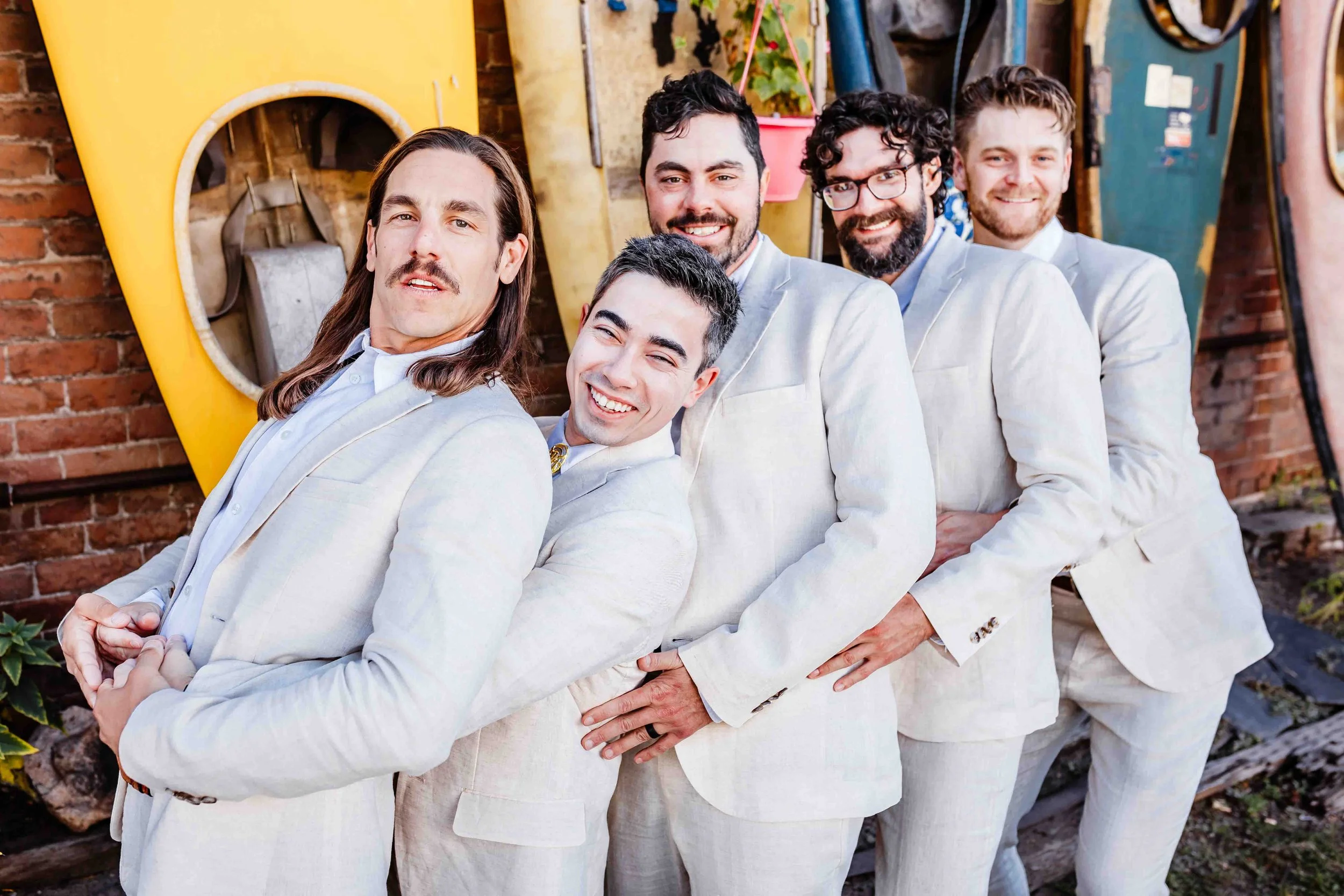 Groom and groomsman posing in a funny way. In Salida, CO in front of the kayak wall holding each others hips all in a conga-line fashion.