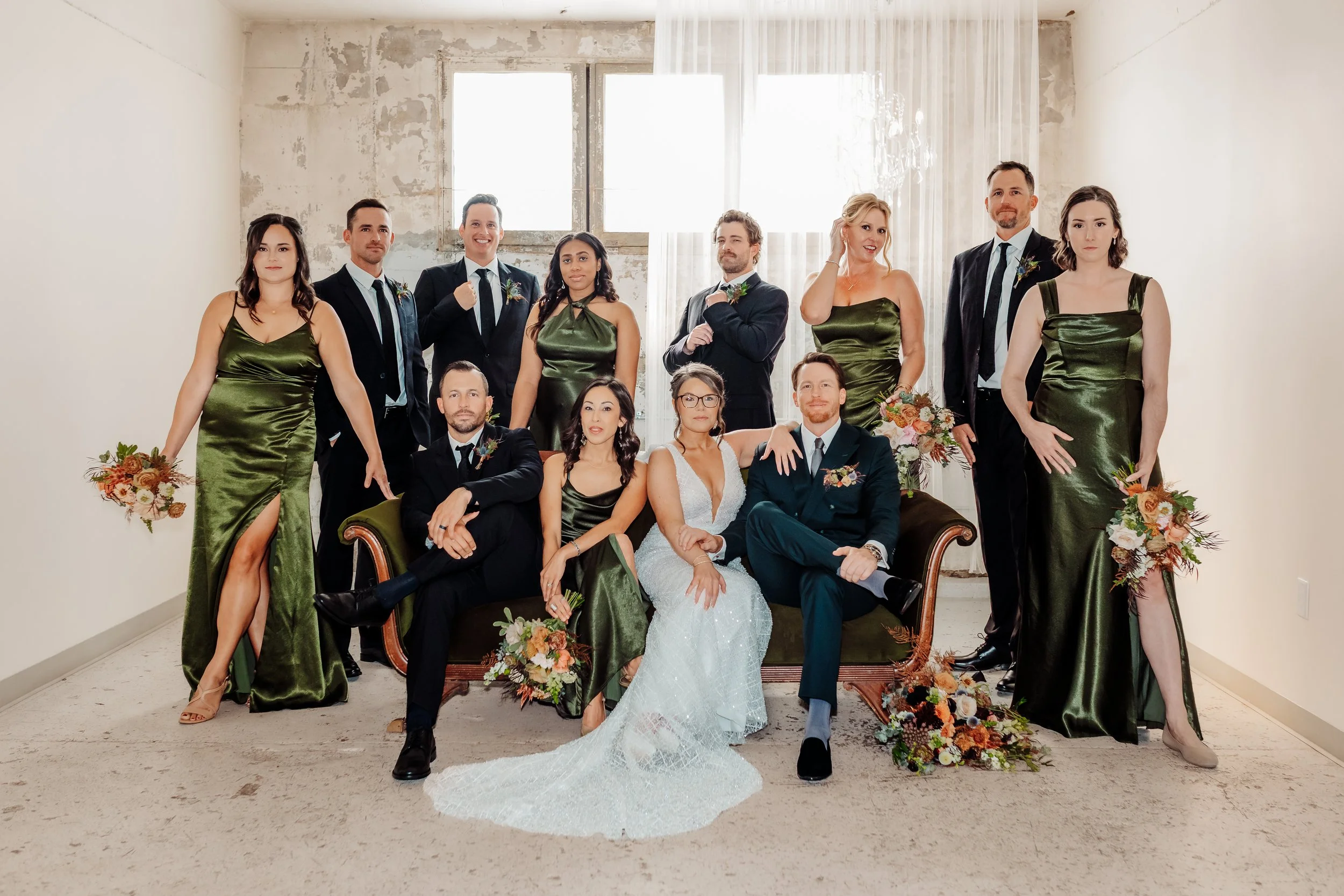 Wedding party at the St. Vrain wedding venue in Longmont CO. Set up in a Vogue like pose, some standing behind green velvet couch, couple sitting elegantly on couch.