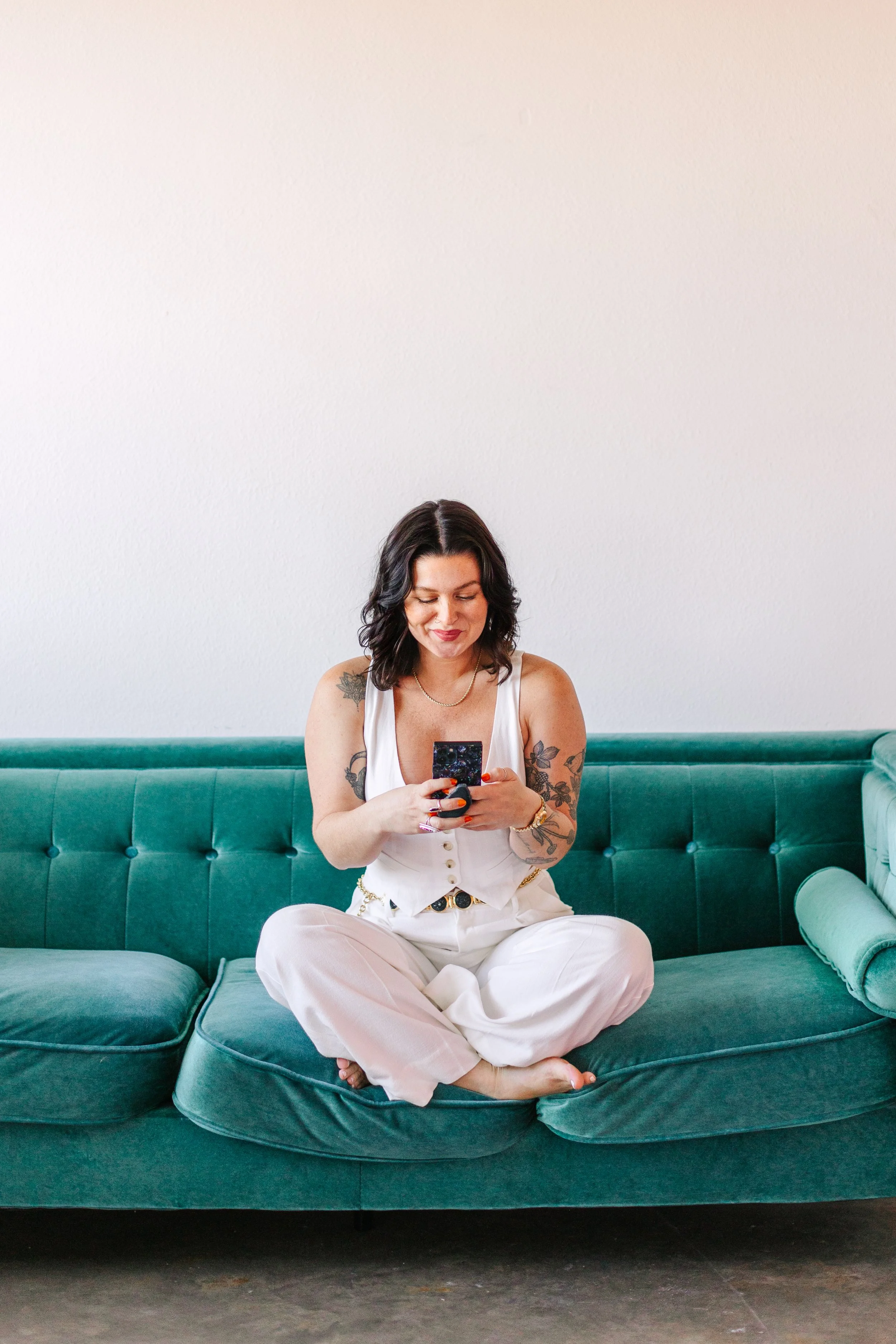Photographer sitting on couch using phone to connect with clients. She looks happy.