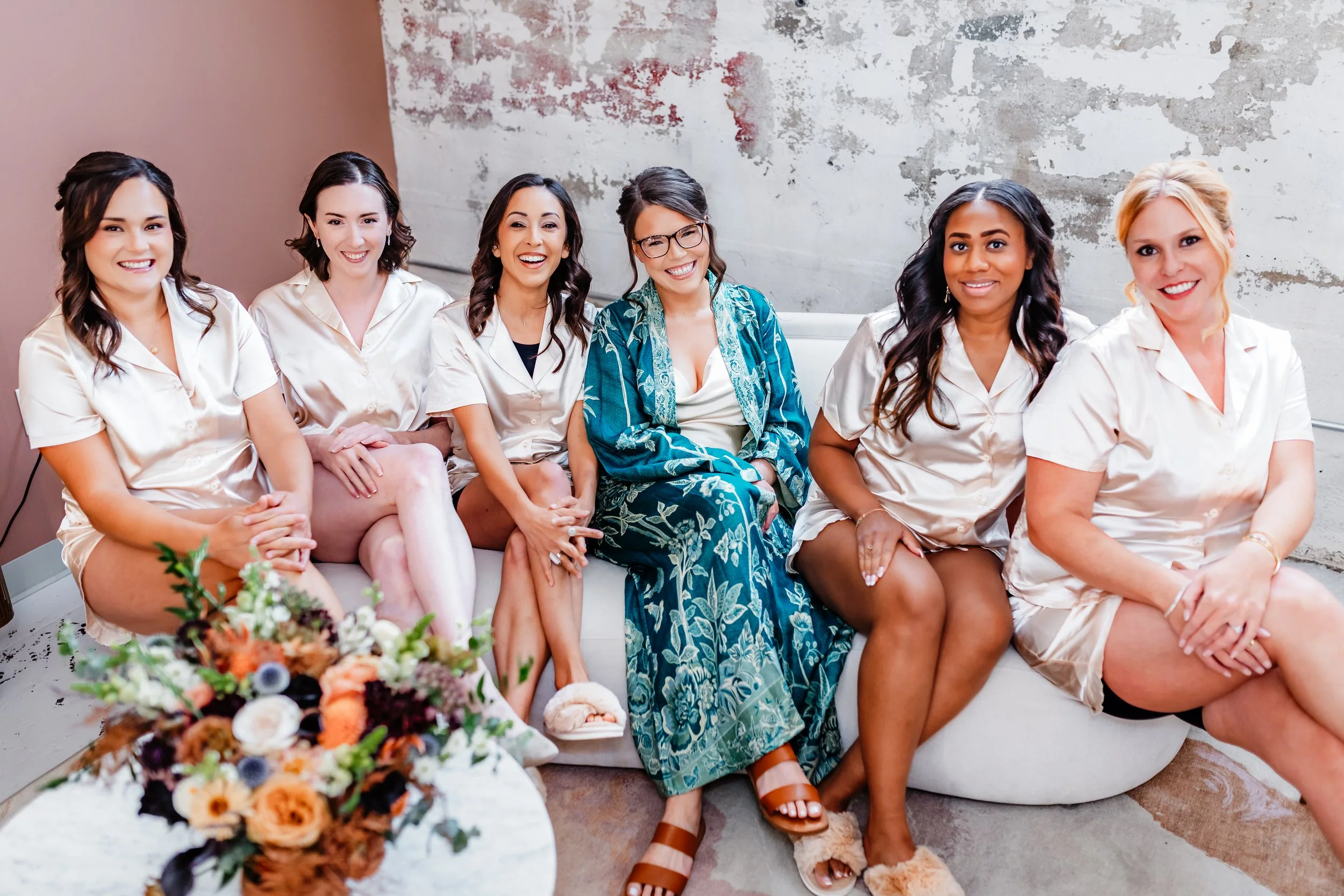 Bride and bridesmaids in getting ready attire at the St. Vrain wedding venue sitting on a couch smiling.