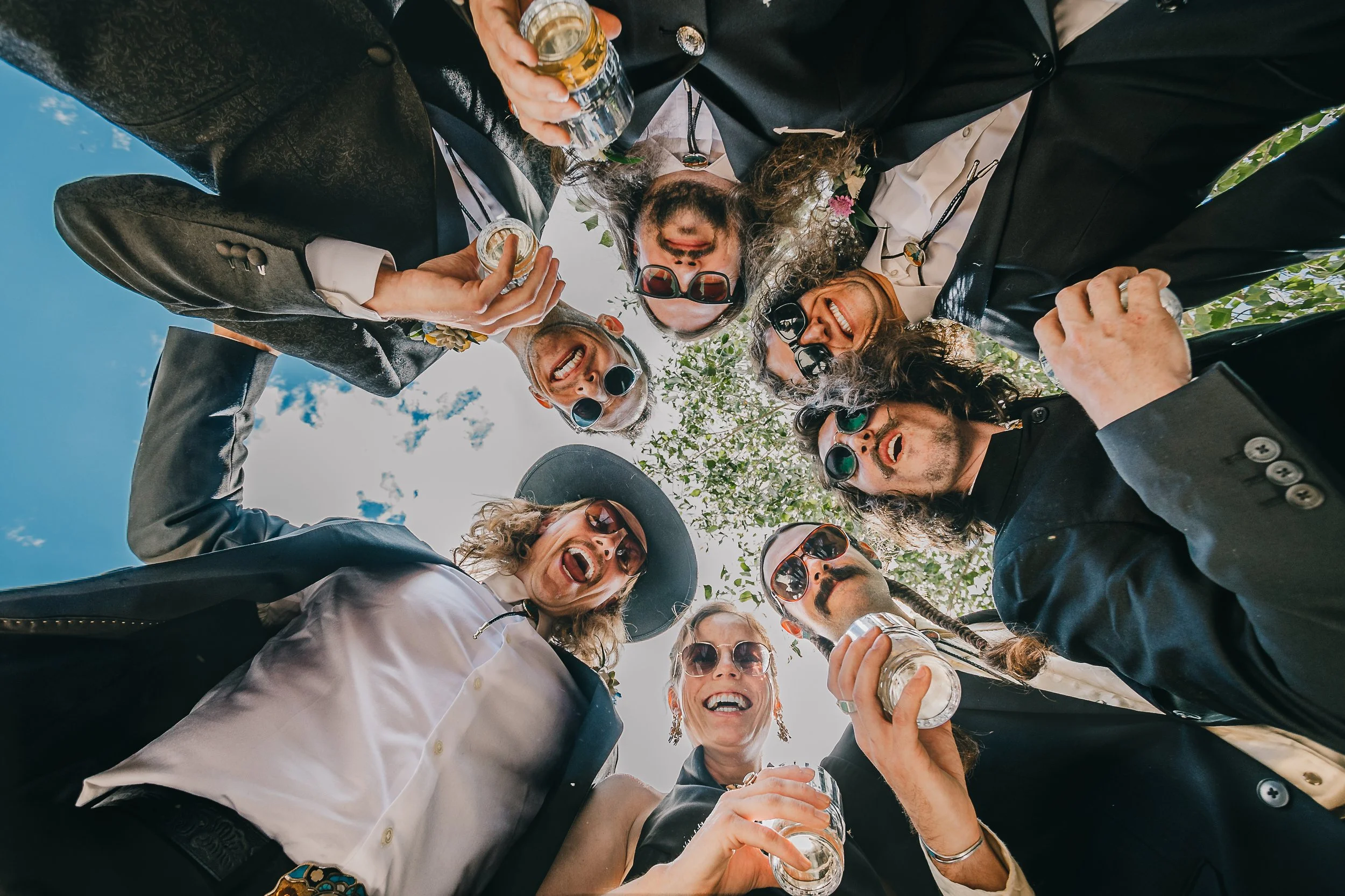 Groomsmen in a circle looking down and into camera. Holding drinks and looking cool and happy.
