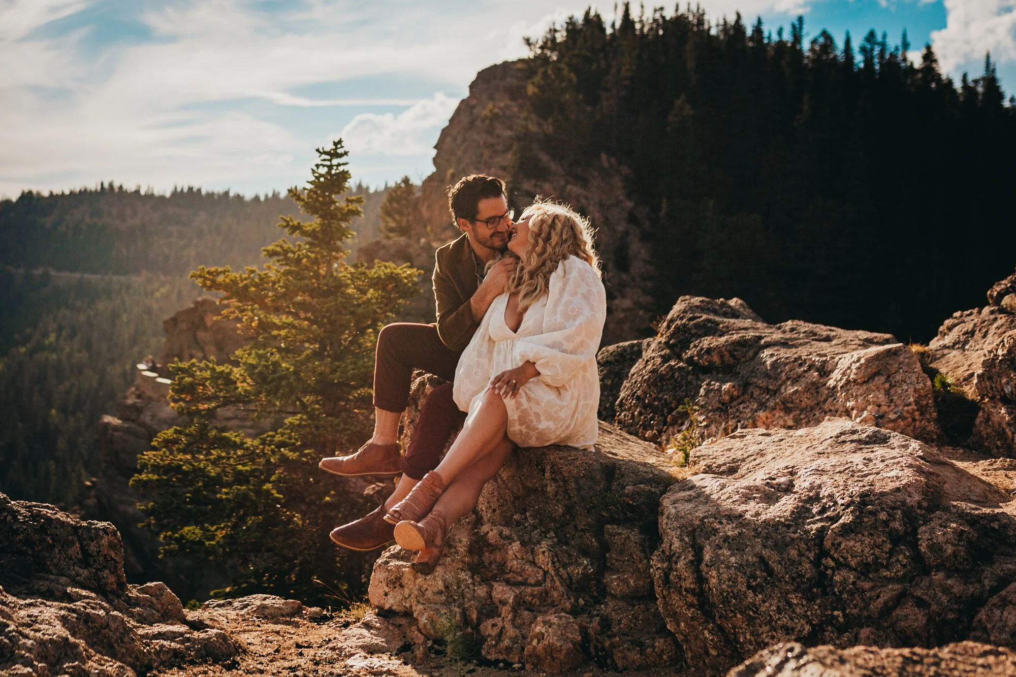 Couple sitting on rocks with mountains in the background at Lost Gulch overlook. Engagement photos.