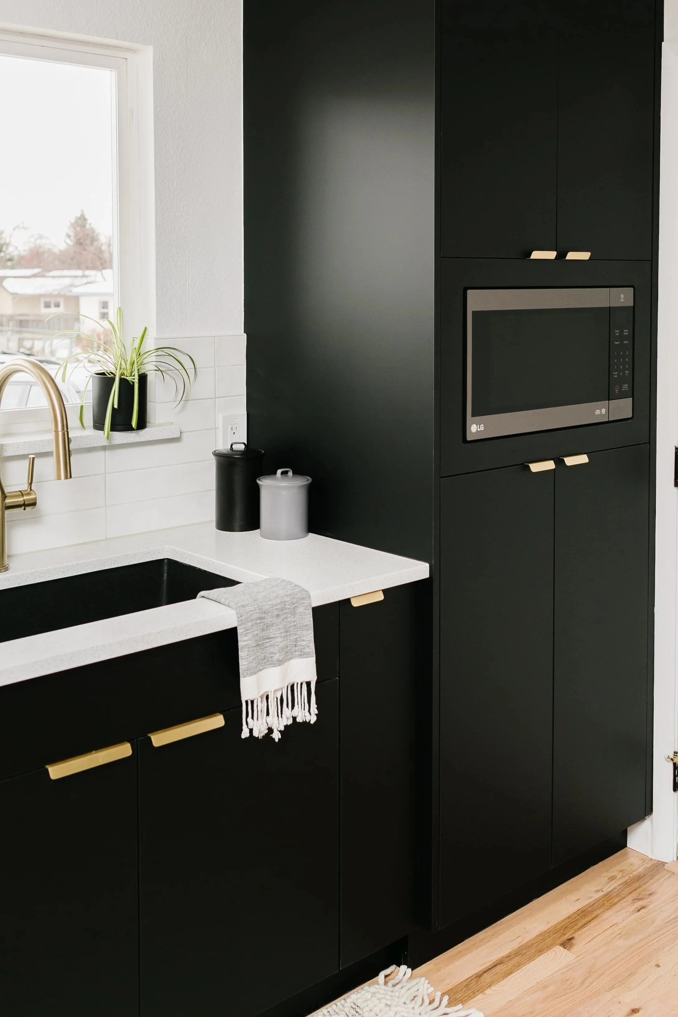 Kitchen with matte flat-paneled cabinetry with gold pulls, white tile backsplash, and white countertop.