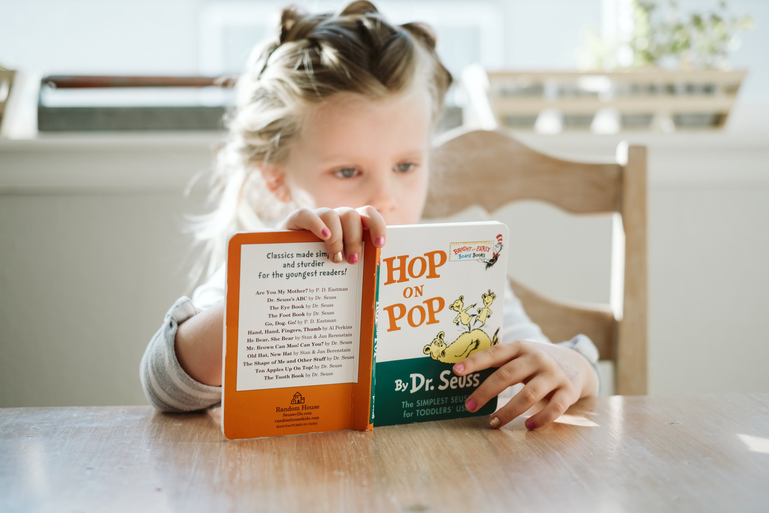 Child reading "Hop on Pop" by Dr. Seuss at a table.