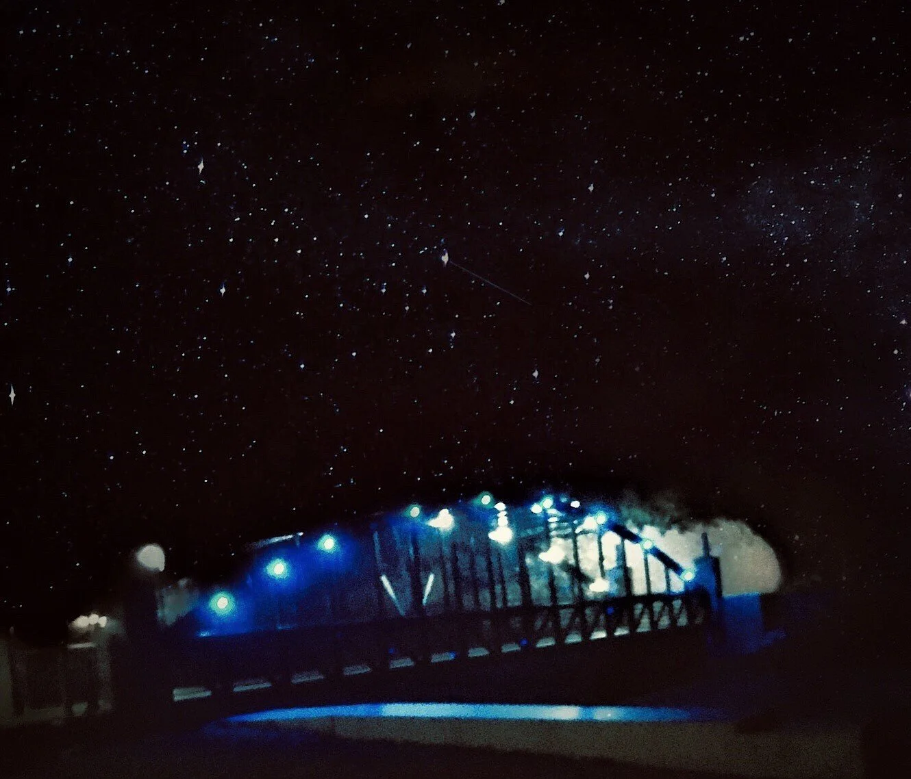 Starry night sky with a bridge illuminated by blue lights