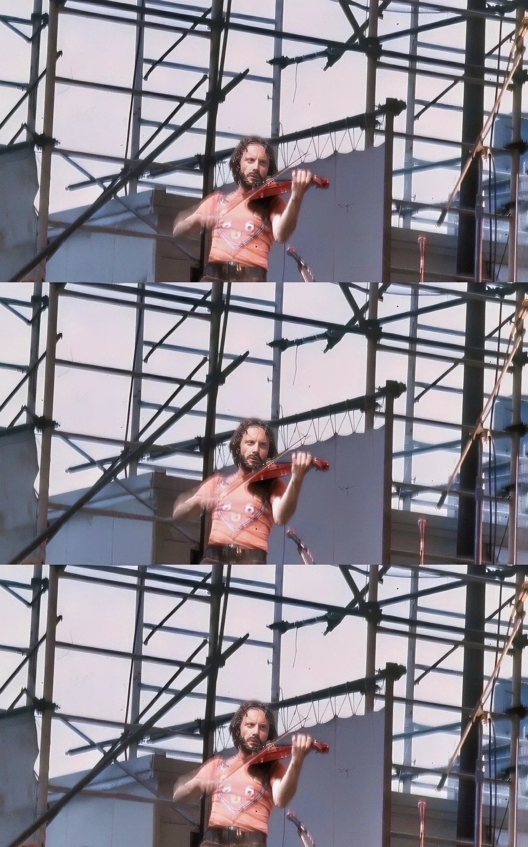 A man with a beard and long hair playing a violin on a rooftop with construction scaffolding and a metal structure in the background.