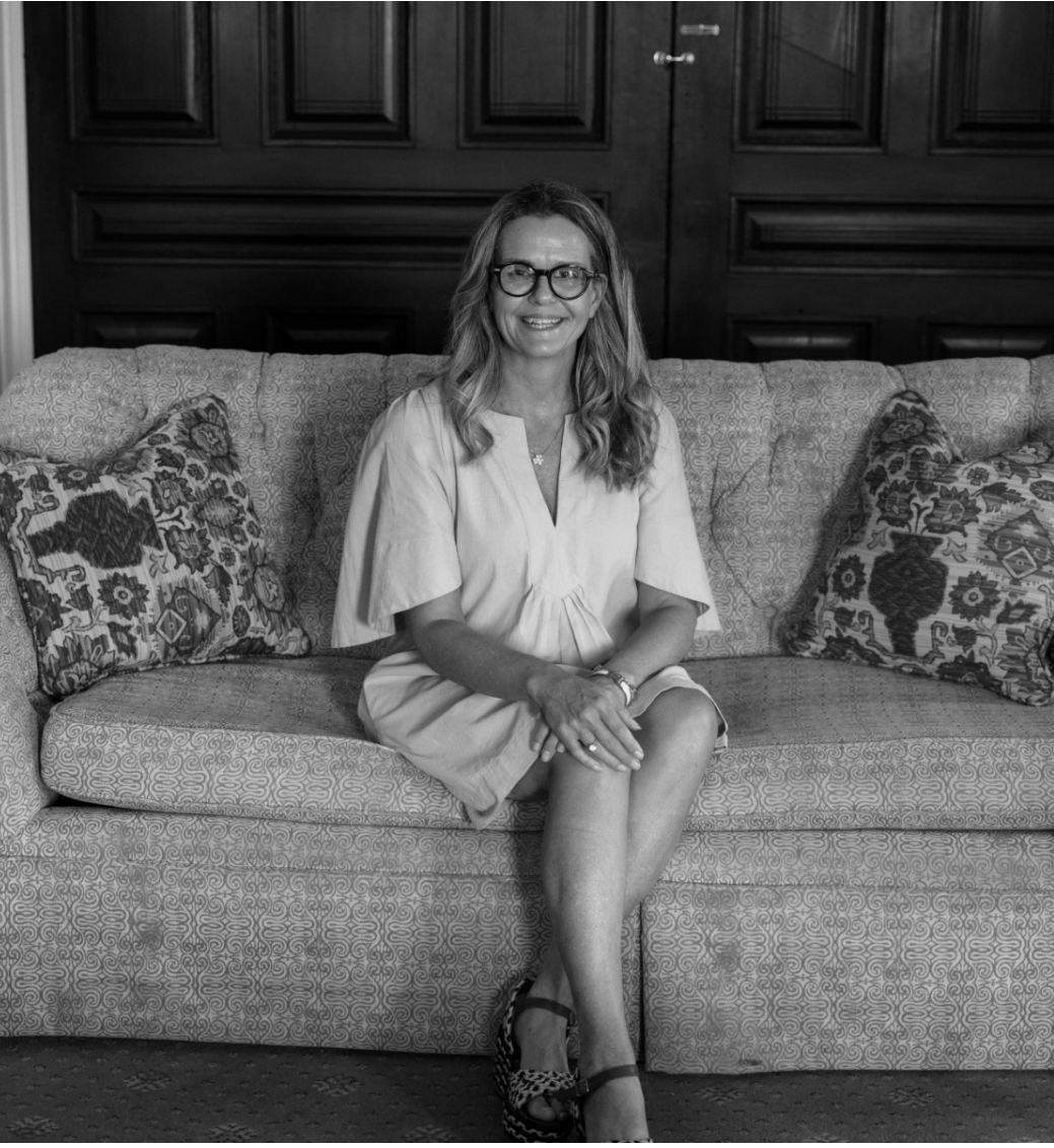 Interior designer Christina Richardson with C Interiors interior design firm, sitting on a patterned sofa with decorative pillows in a room with dark wood paneled walls.