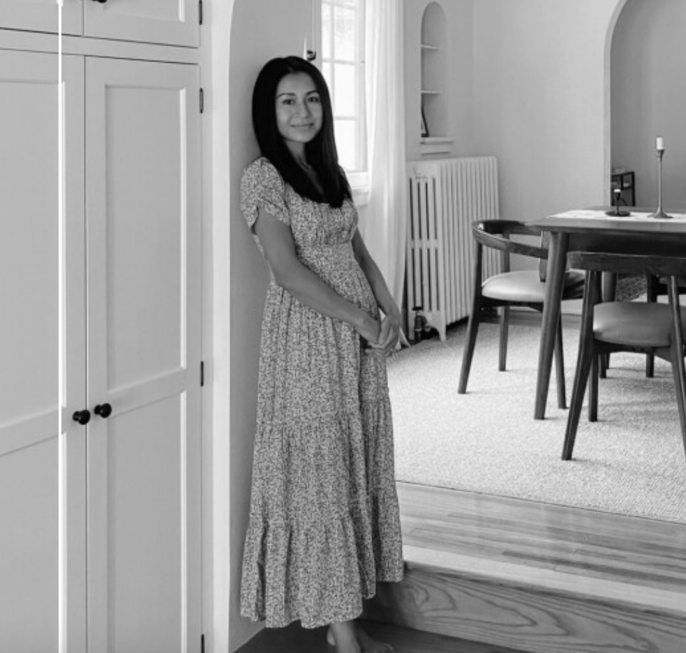 Interior Designer and home decor influencer Patti Wagner with PatticakeWagner.com in a floral dress standing in a living room, near a closet and a radiator, with a dining table and chairs in the background.