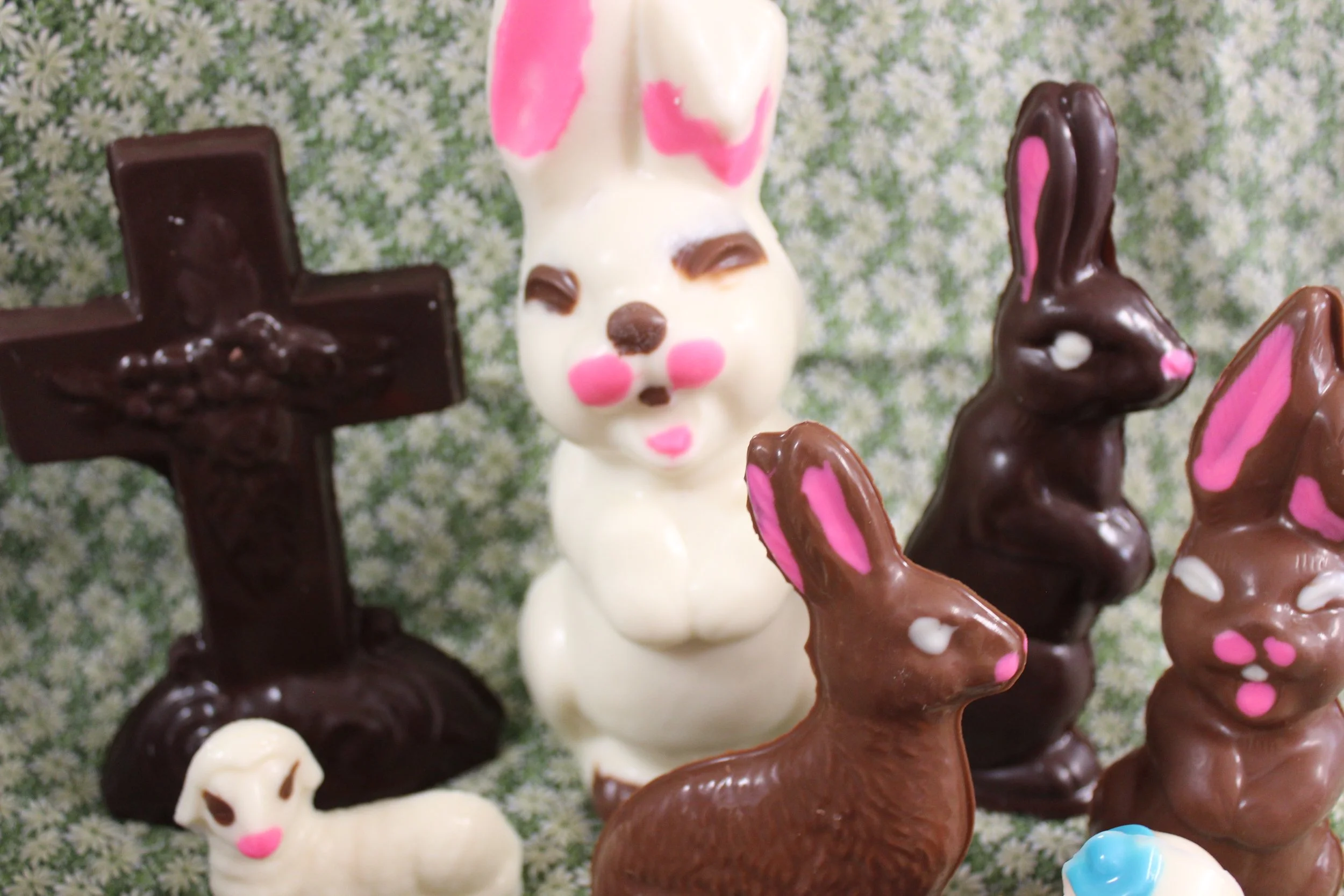 Various chocolate and white chocolate Easter bunny and cross decorations on a floral background.