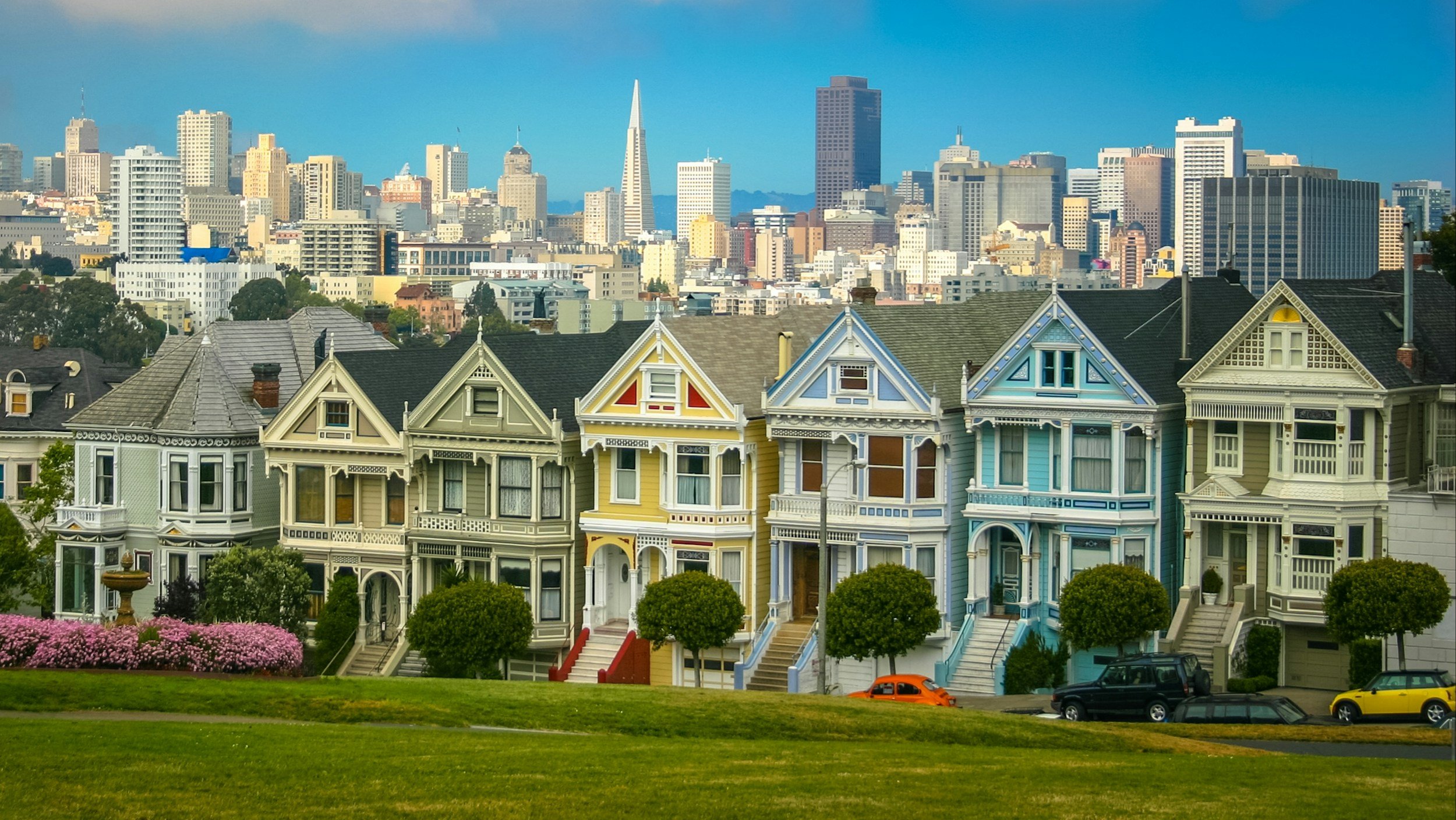 Colorful Victorian houses on a hillside in San Francisco with the downtown skyline in the background.