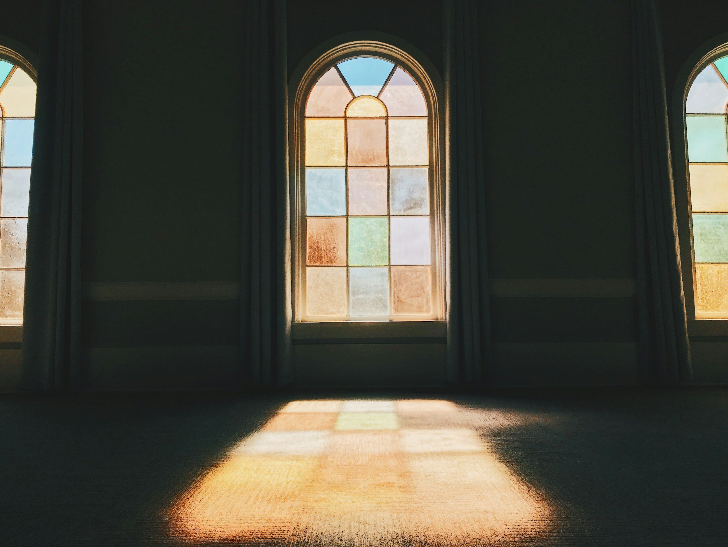 Sunlight coming through stained glass windows, casting colorful light and shadow on the floor inside a room.