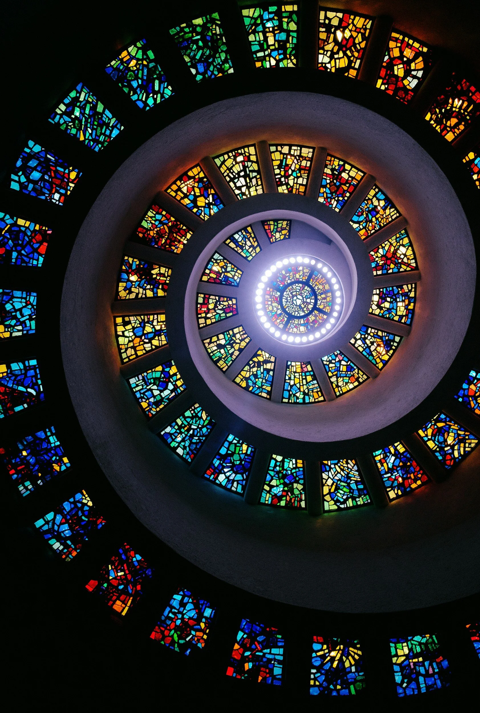 Colorful stained glass spiral window viewed from below, creating a mesmerizing spiral pattern of vibrant mosaic pieces in various colors.