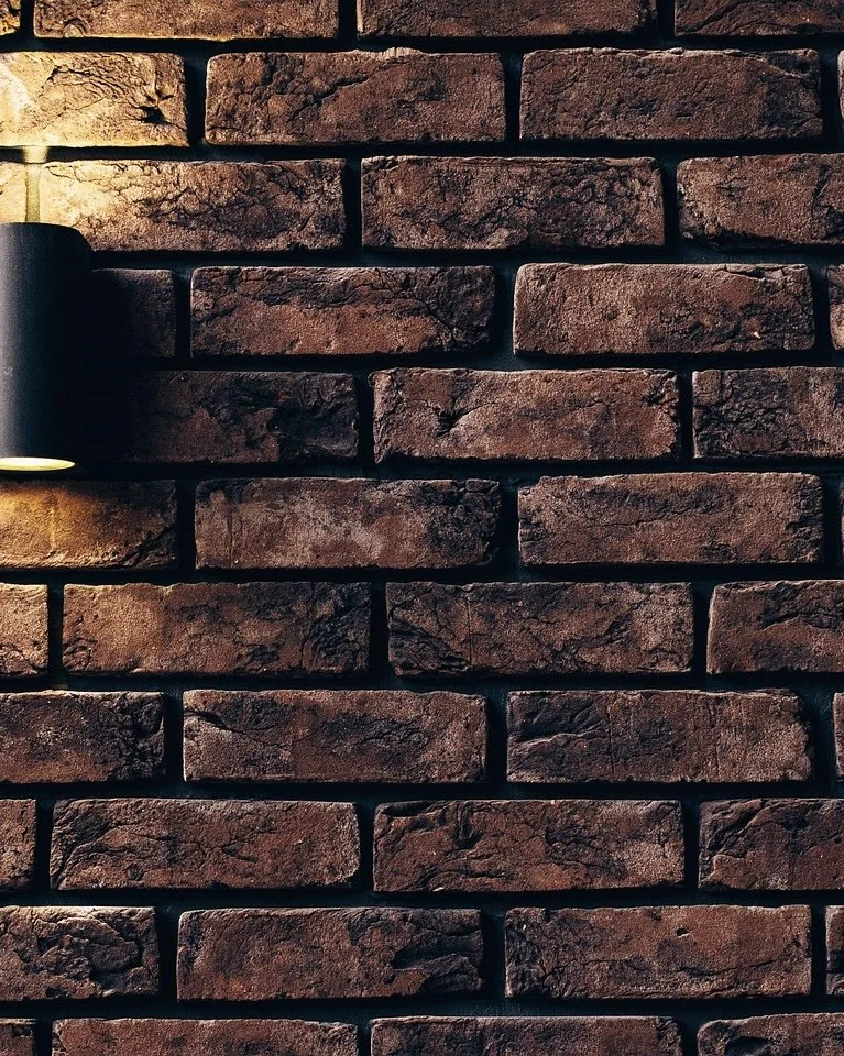 Close-up of a brick wall with a wall-mounted black light fixture casting warm light on the bricks.