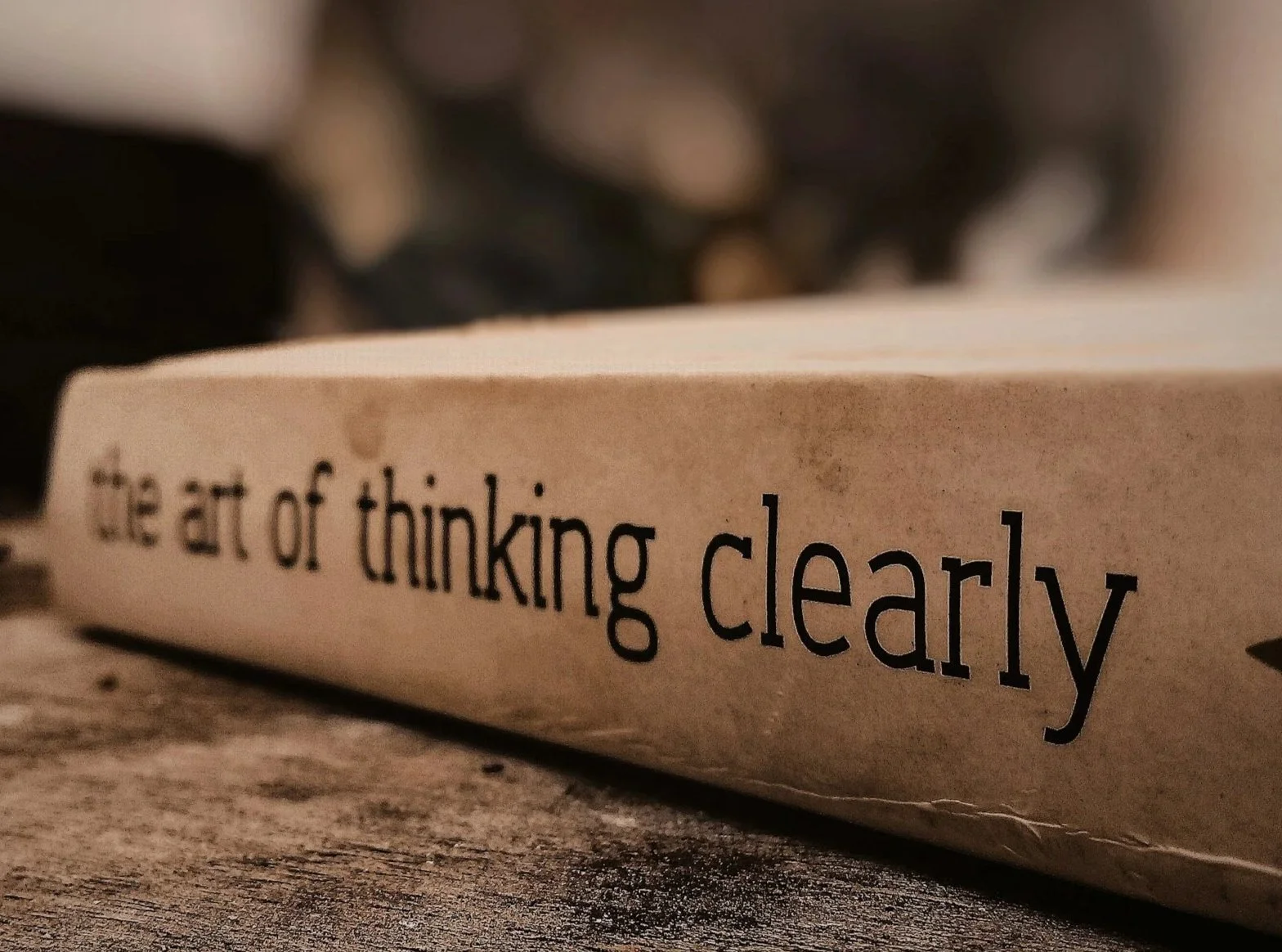 Close-up of a book with the words 'the art of thinking clearly' on the spine, resting on a wooden surface, with blurred background.