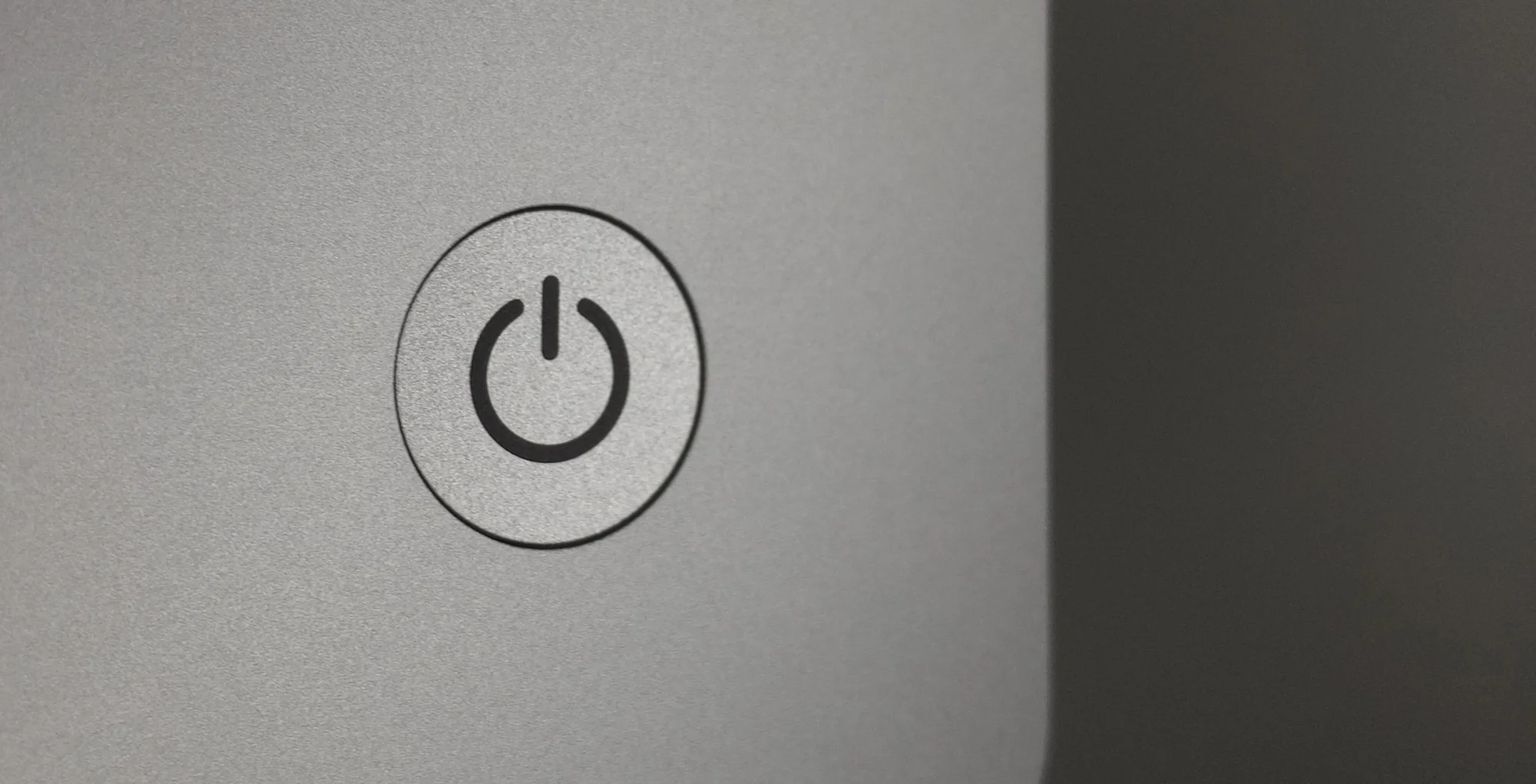 Close-up of a power button icon on a gray surface, likely on an electronic device.