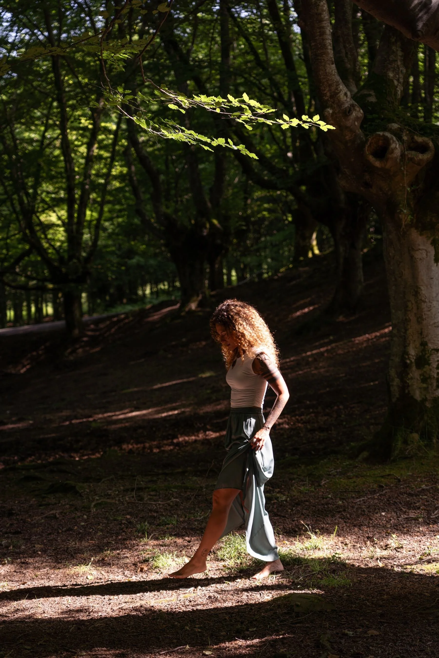 Mujer caminando descalza por el bosque entre árboles y sombras.