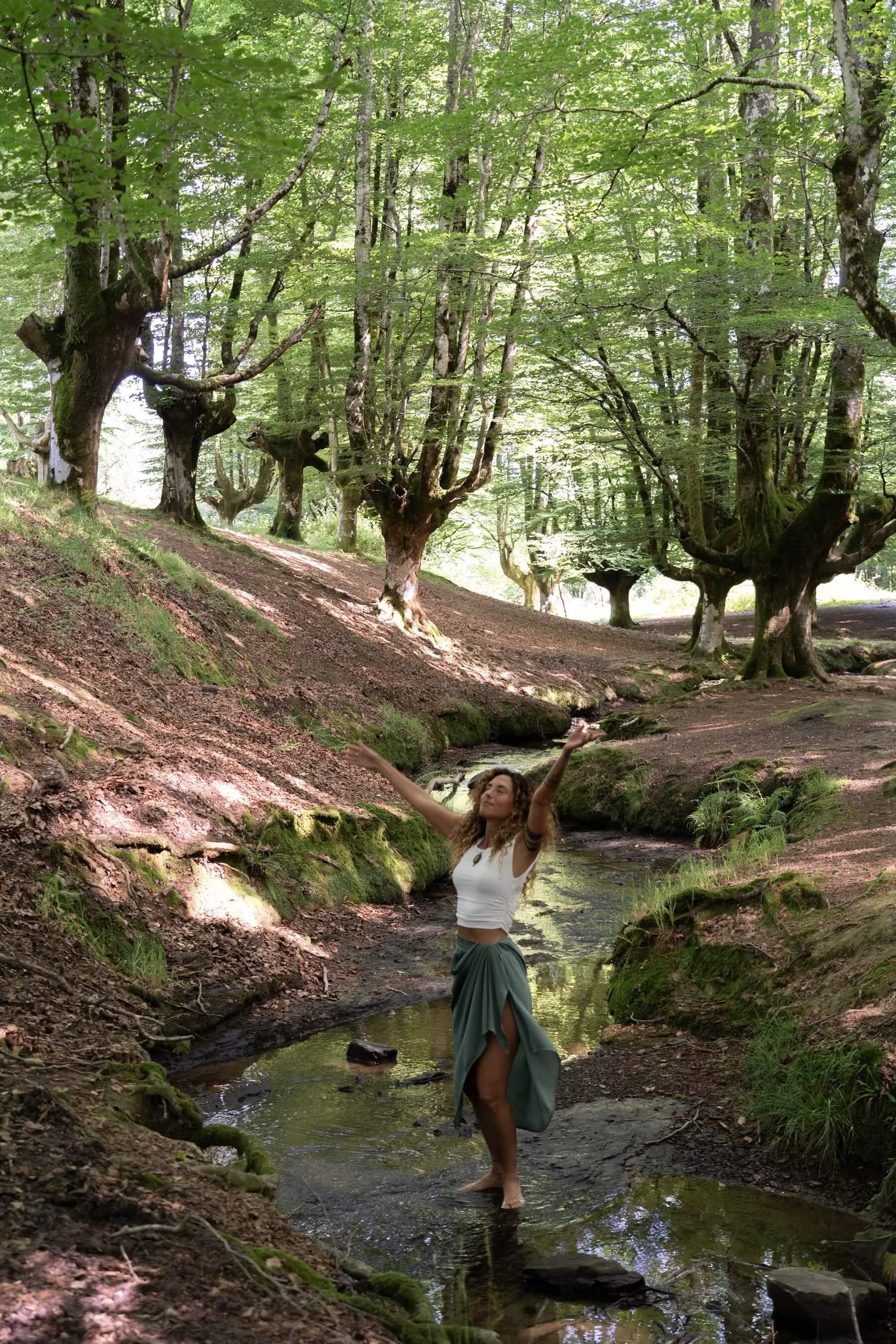 Ana disfrutando en un río rodeada de árboles frondosos en un bosque.