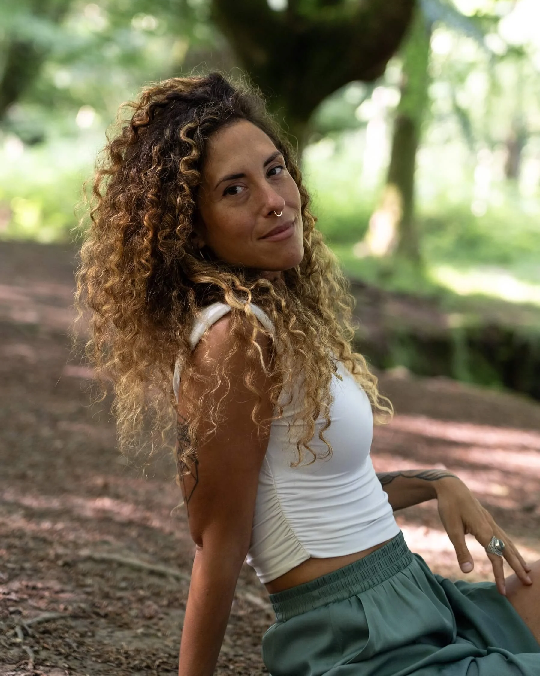 Ana sentada en la hojarasca, en un bosque, mira y sonrie a la cámara
