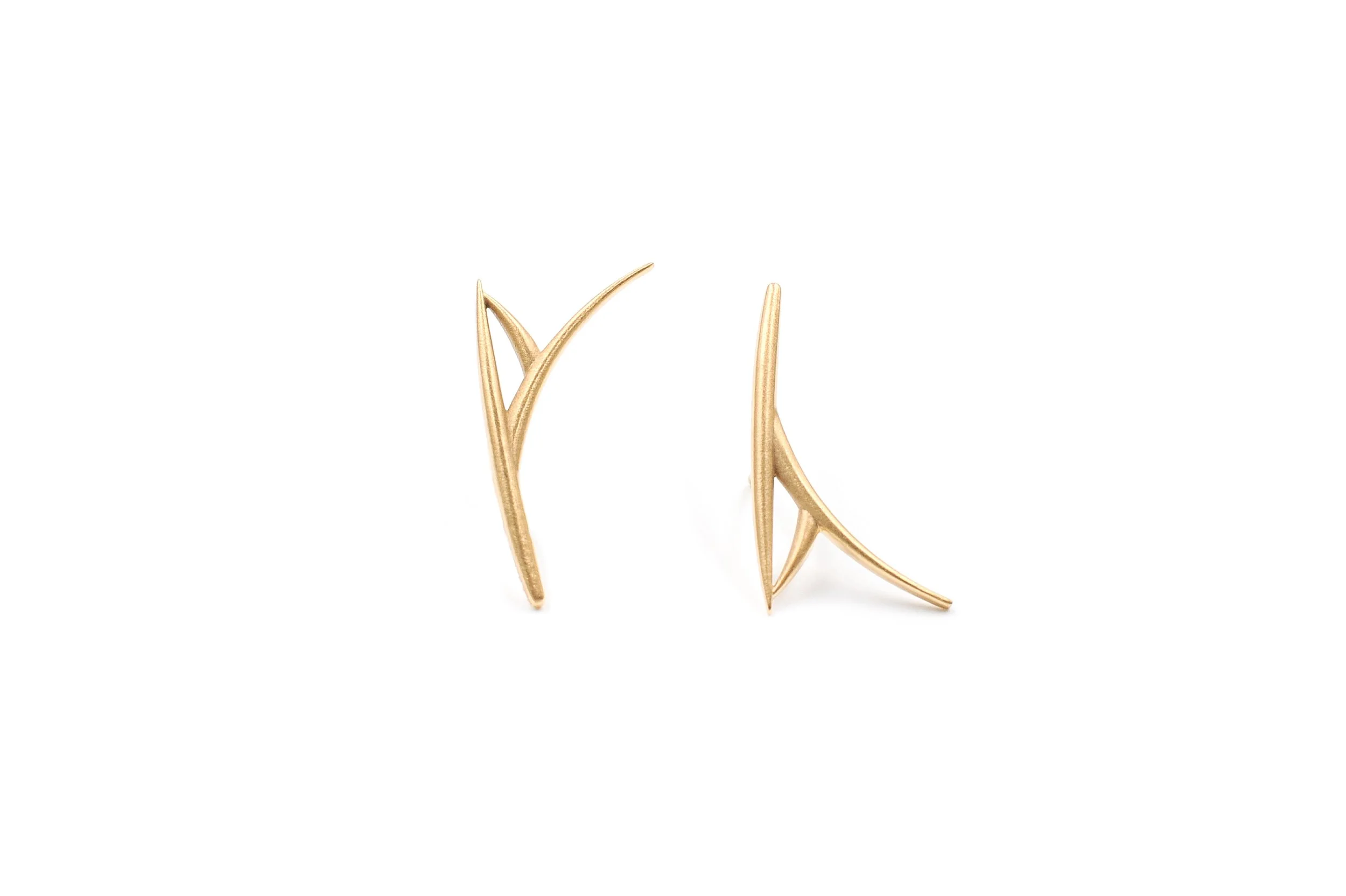 Gold earrings with elongated, curved, and pointed design, placed on a white background.