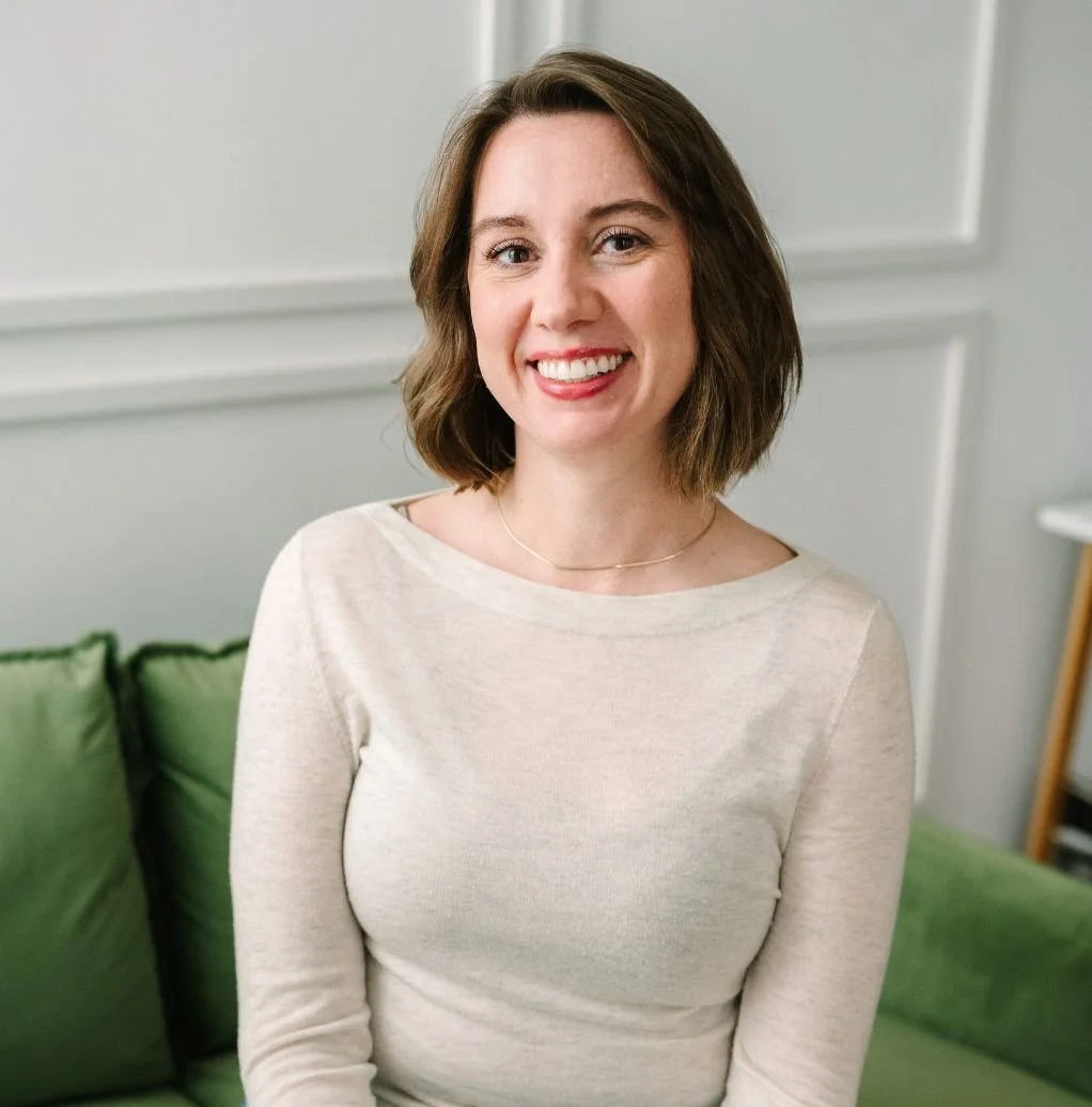 Person smiling at a desk with a laptop and smartphone, blue wall background, office setting.