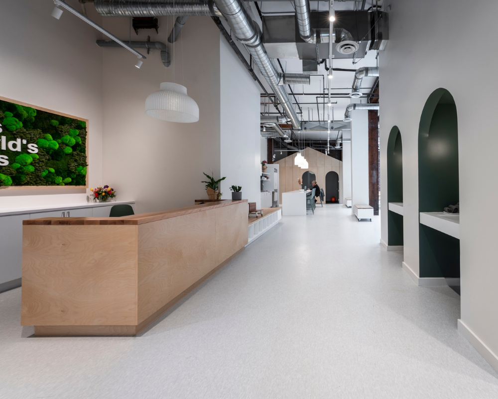 Bright reception area at This World’s Ours Centre in Vancouver, BC, featuring a wood reception desk, moss wall artwork, modern lighting, and a spacious hallway with therapy rooms.