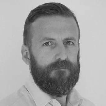 Black and white portrait of bearded man with slicked-back hair, looking at the camera.