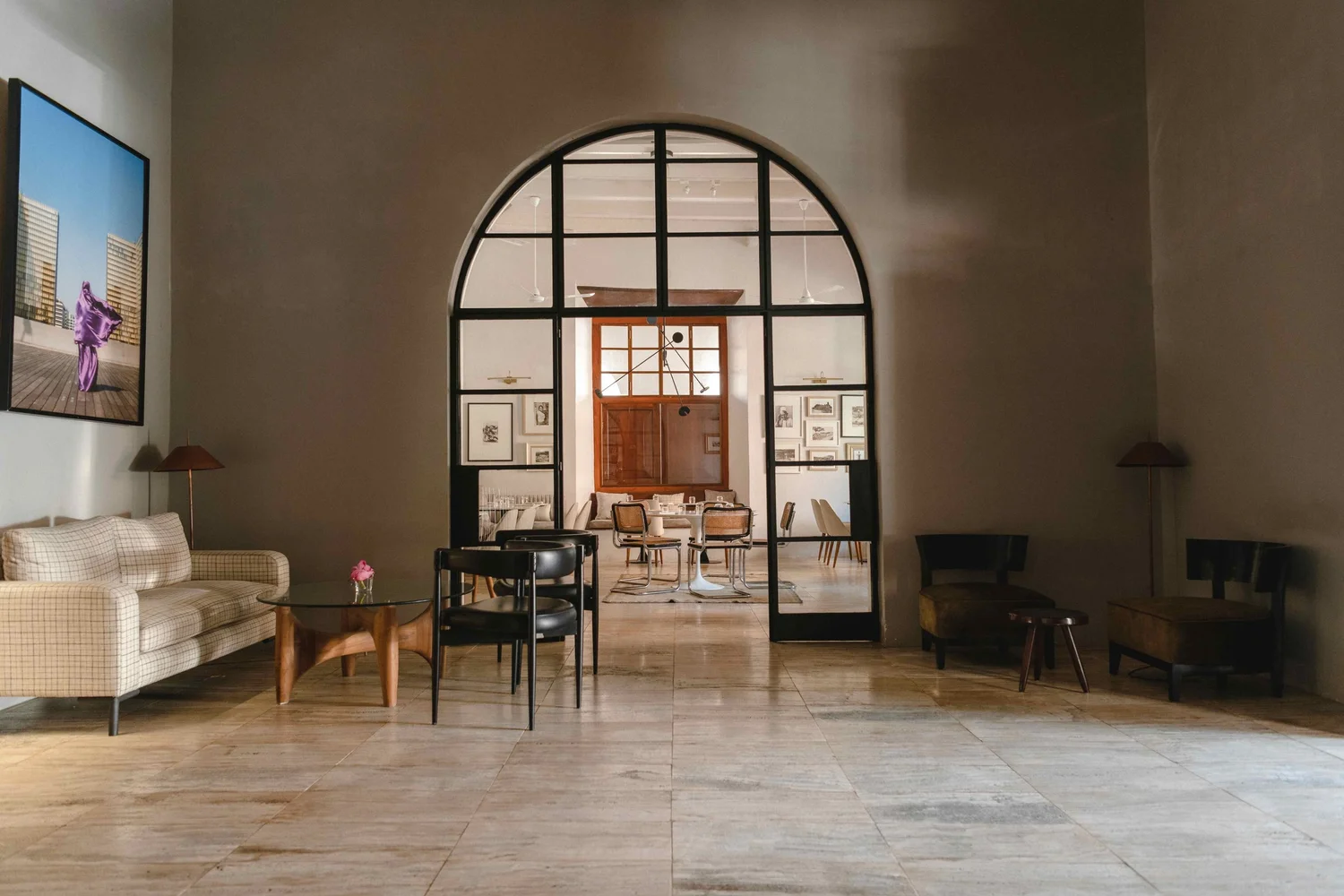 A sitting room with a cream sofa and a round table, and an arched steel-framed glass door through to the next room