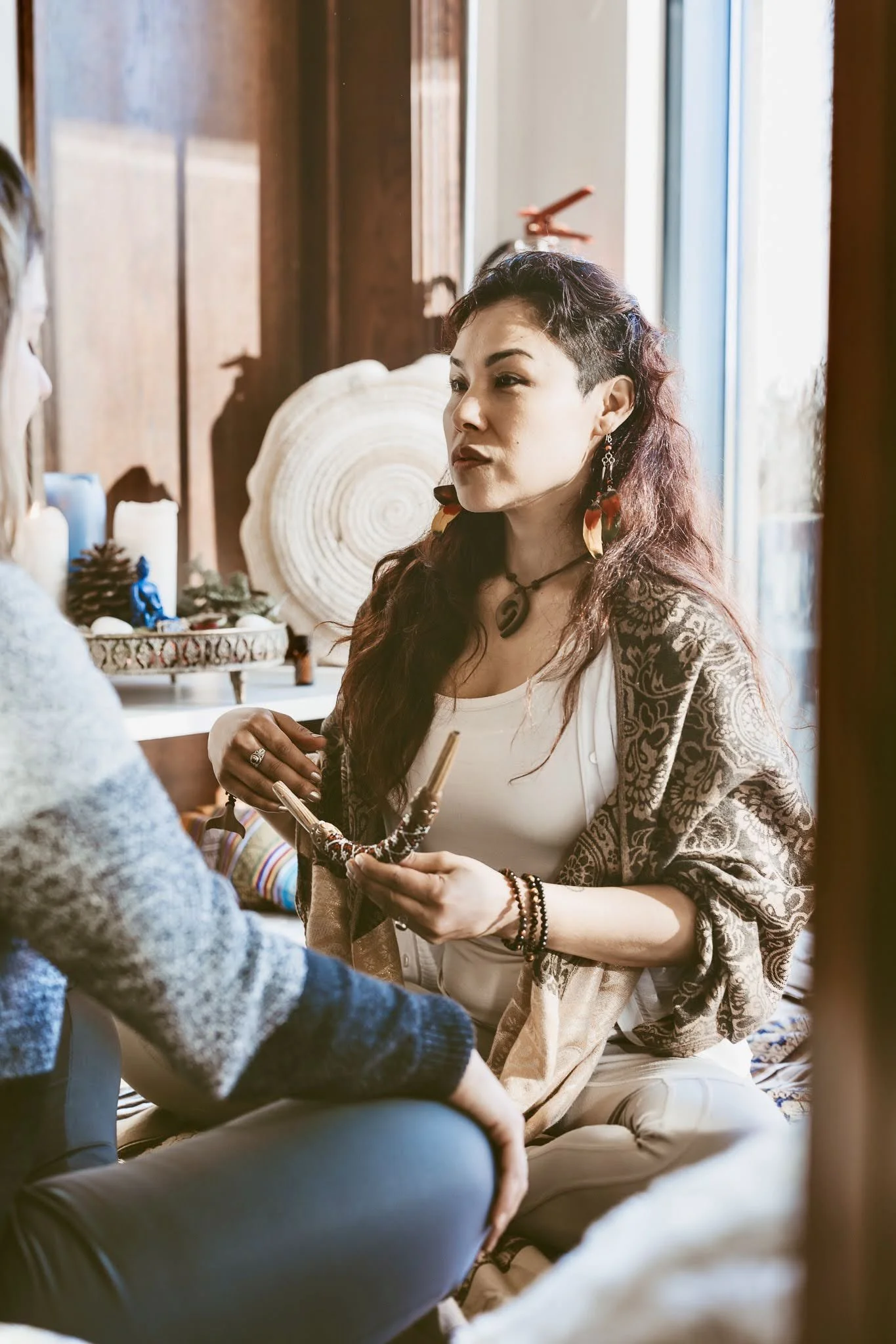 A woman with long curly hair and patterned shawl engaging in a conversation indoors, with candles and decorative items in the background.