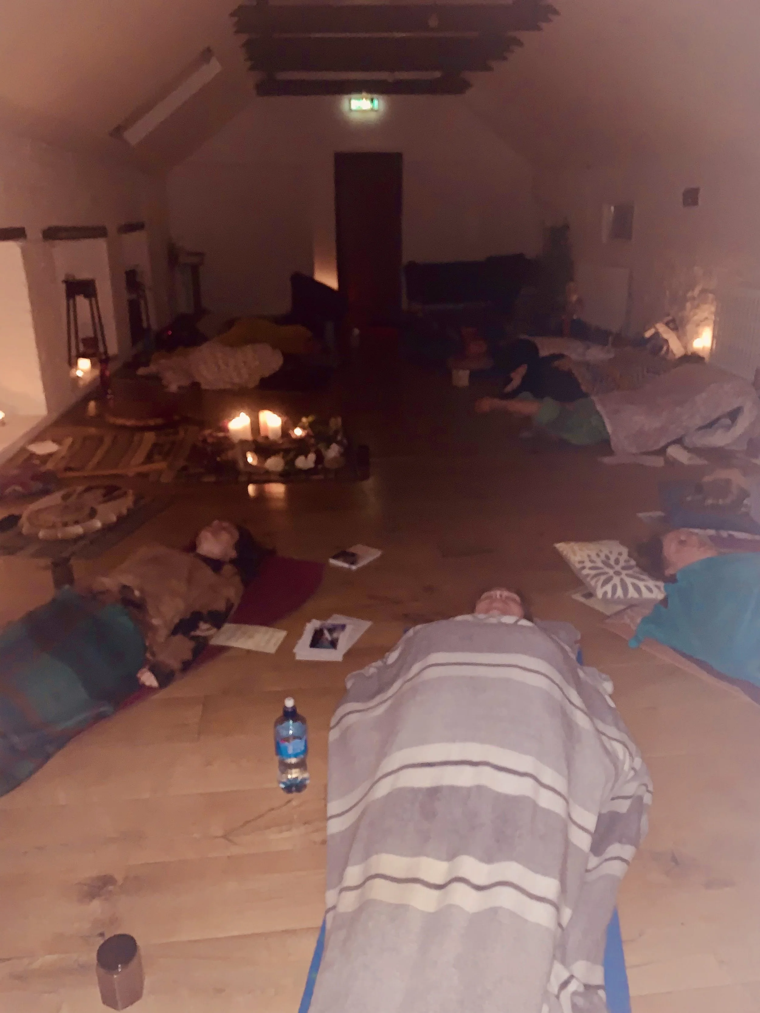 People lying on the floor in a dimly lit room with candles, some blankets, and scattered photos.