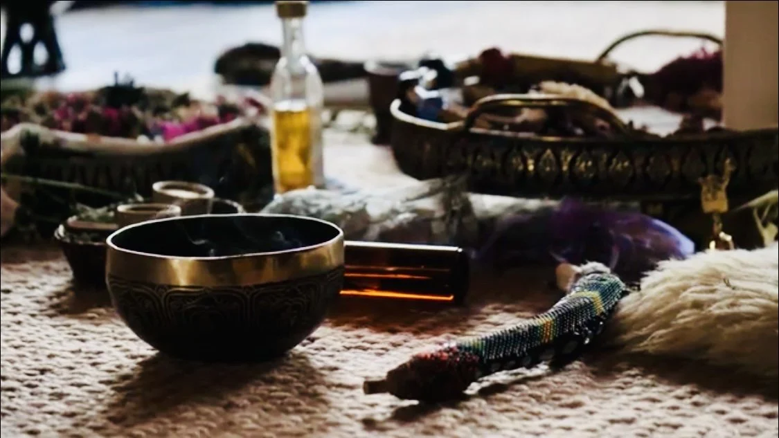 Various jewelry, bowls, and baskets placed on a textured surface, with a hanging bead necklace and a flute, in a setting with natural light.