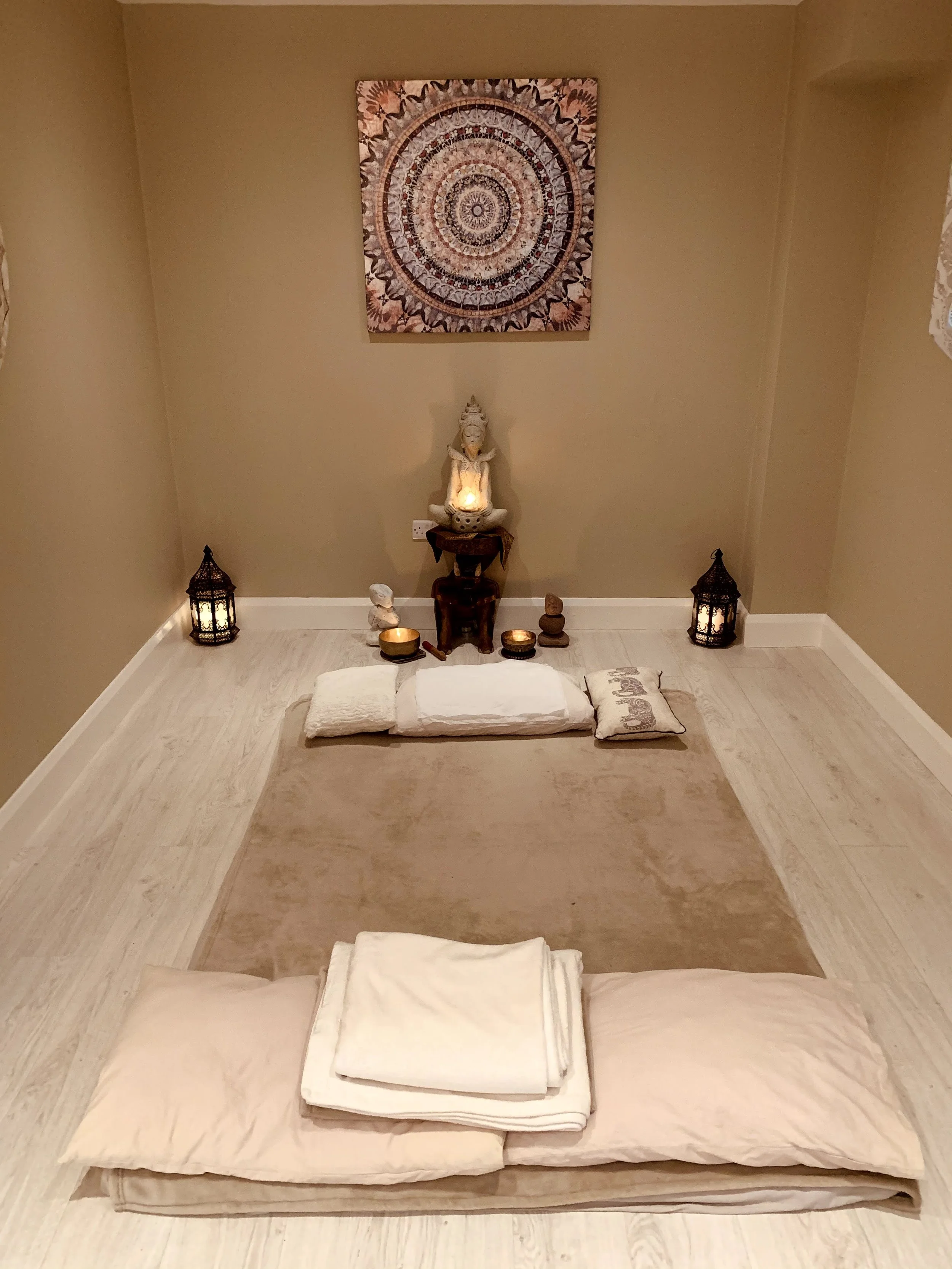 A meditation or prayer space with a floor-level bedding setup, pillows, and calming decorative elements, including candles and a Buddha statue, in a cozy room.