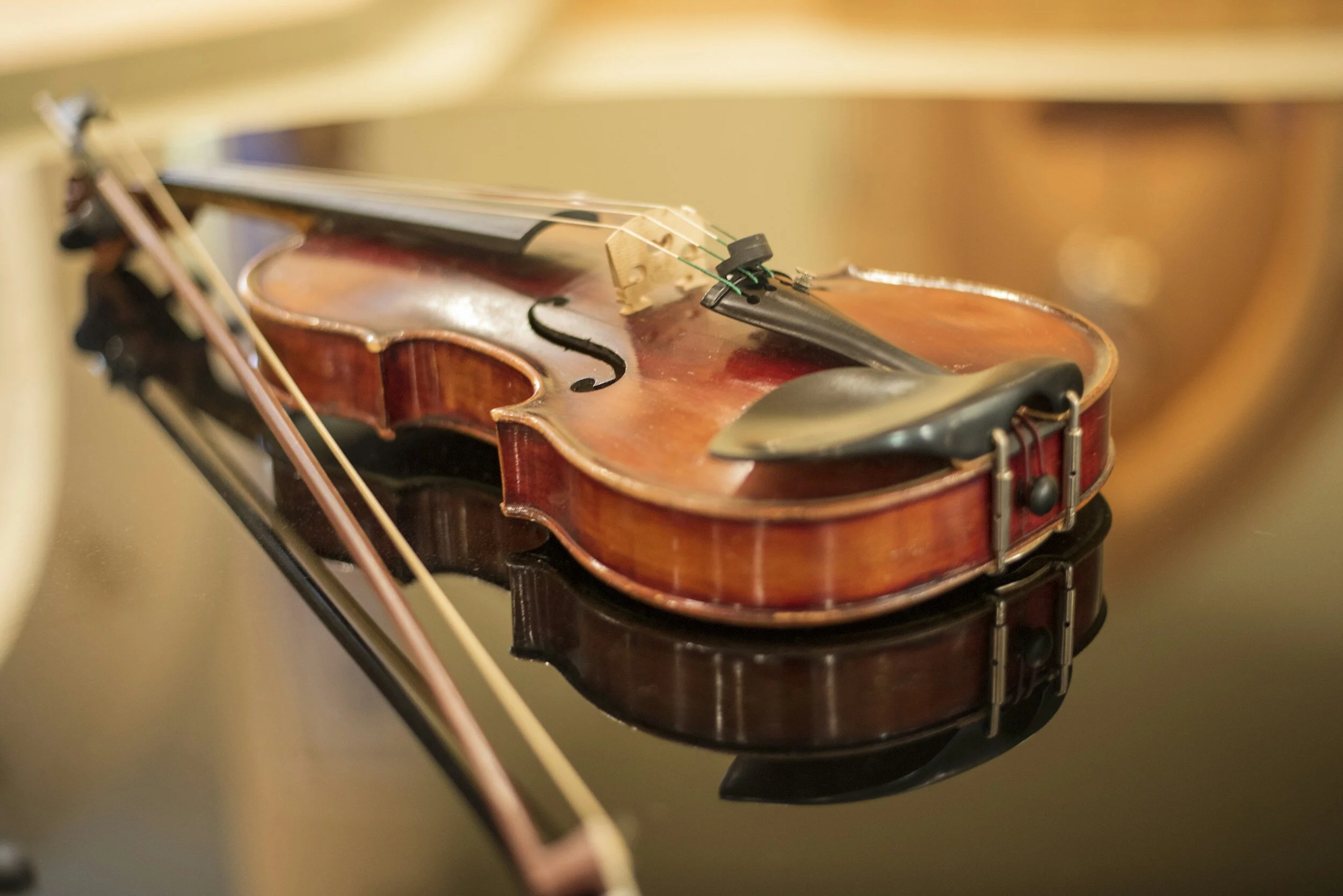 A wooden violin resting on a reflective black surface, with its bow laying beside it.