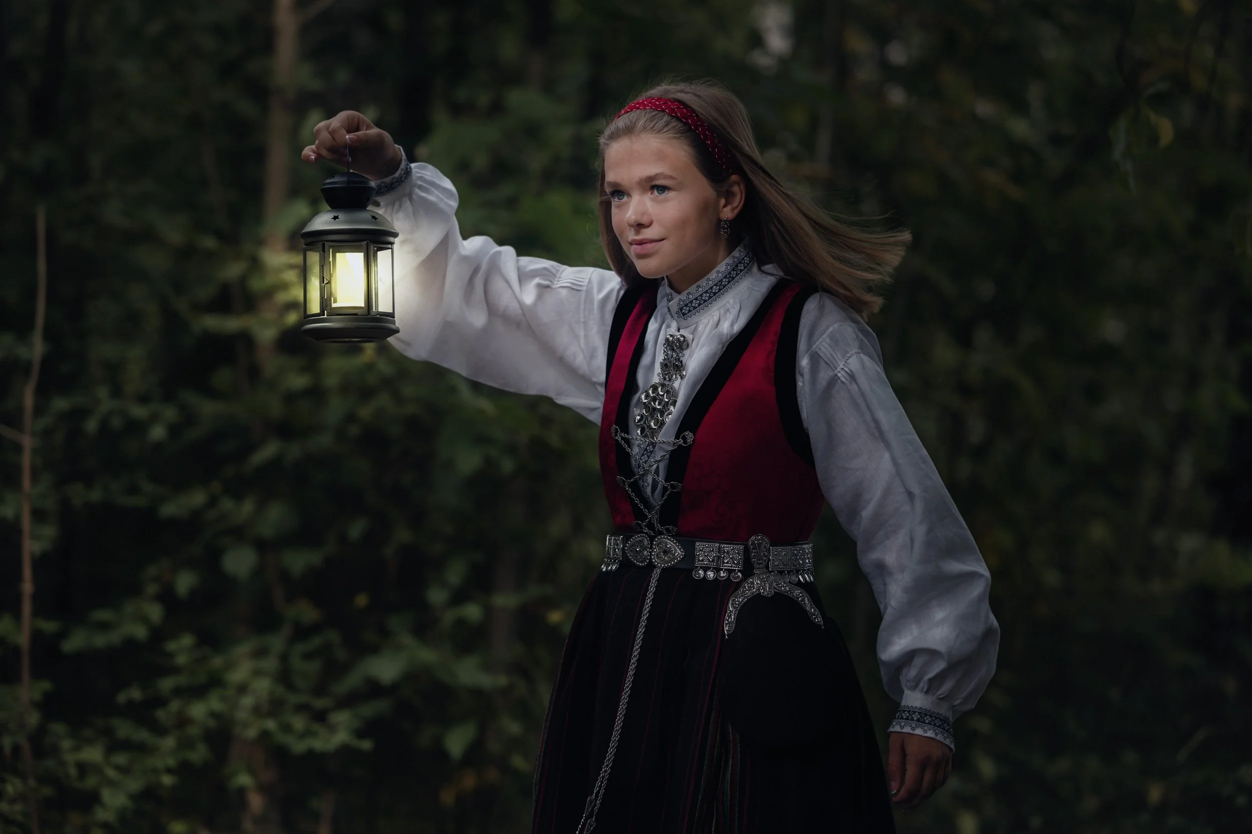 Konfirmant  i tradisjonell norsk kle, holder en lommelykt i skogen om kvelden.