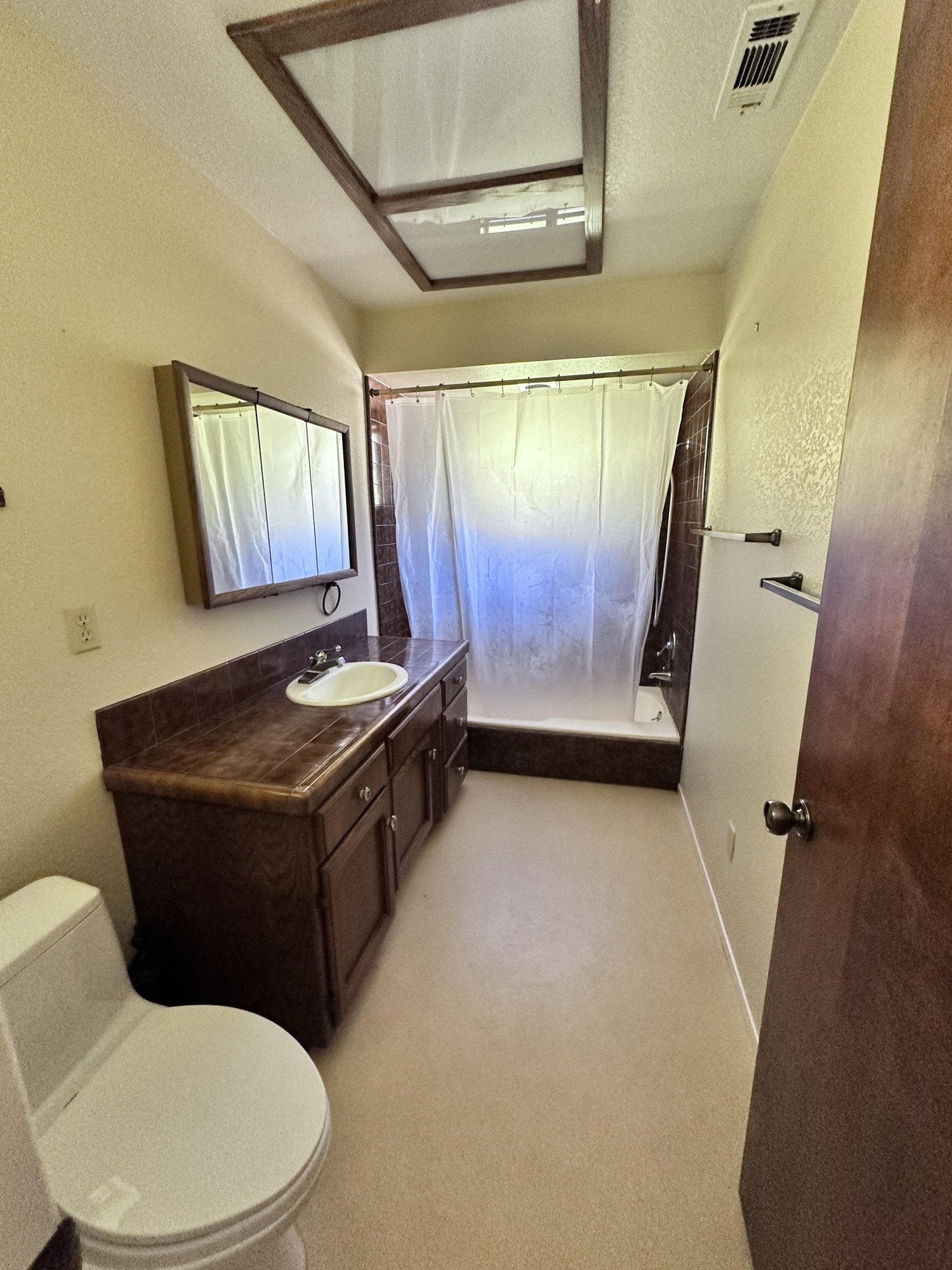 Bathroom before remodel with tile vanity, tub shower, skylight, and older finishes