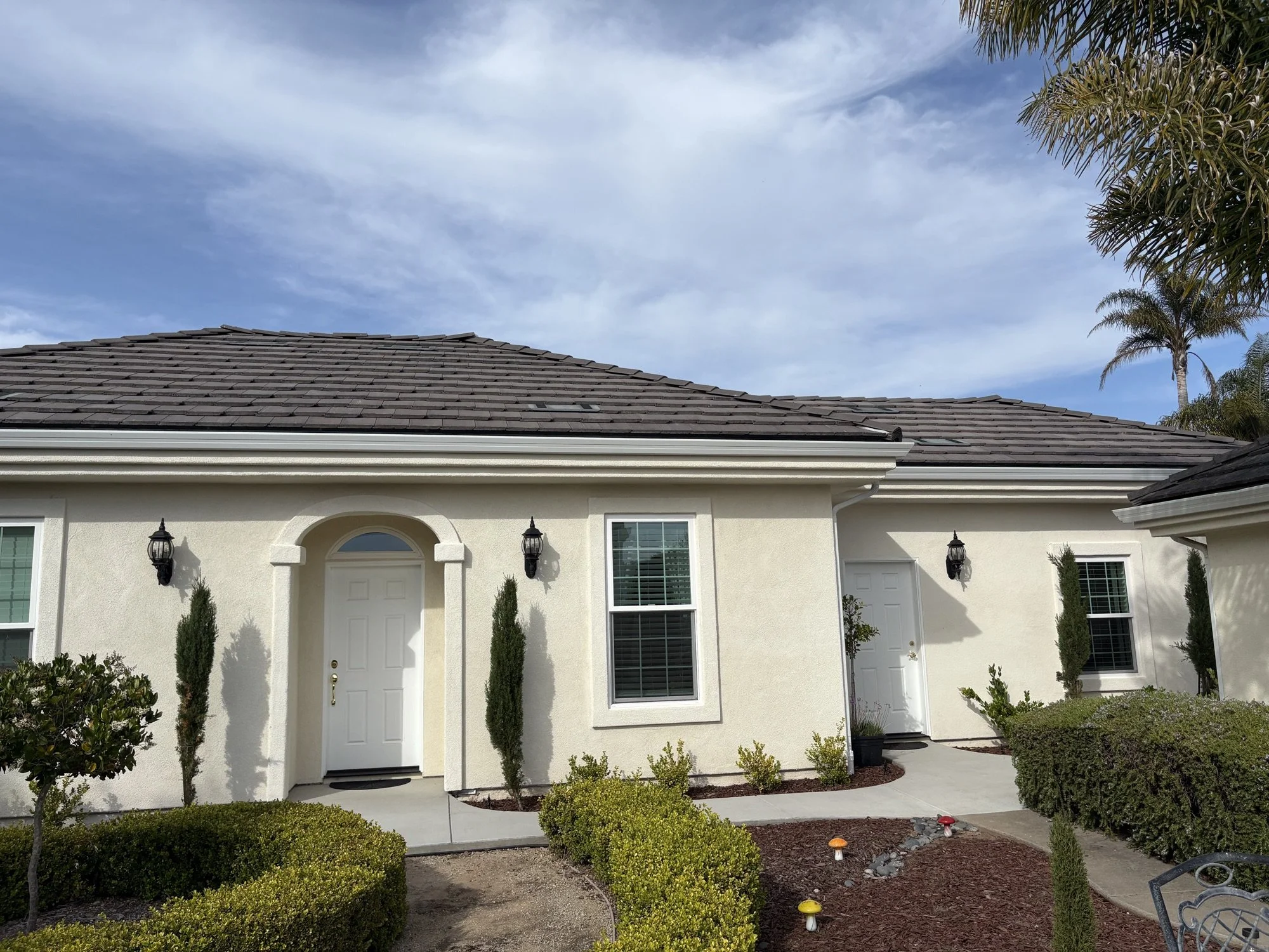 Exterior home remodel detail with stucco entry, upgraded windows, landscaping, and tile roof