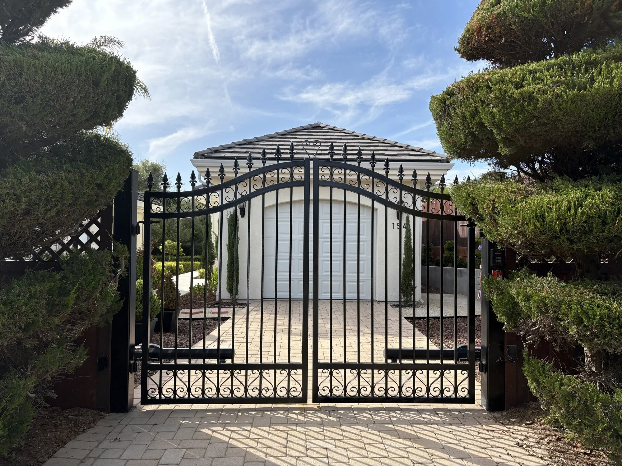 Custom black metal driveway gate leading to a finished residential exterior project