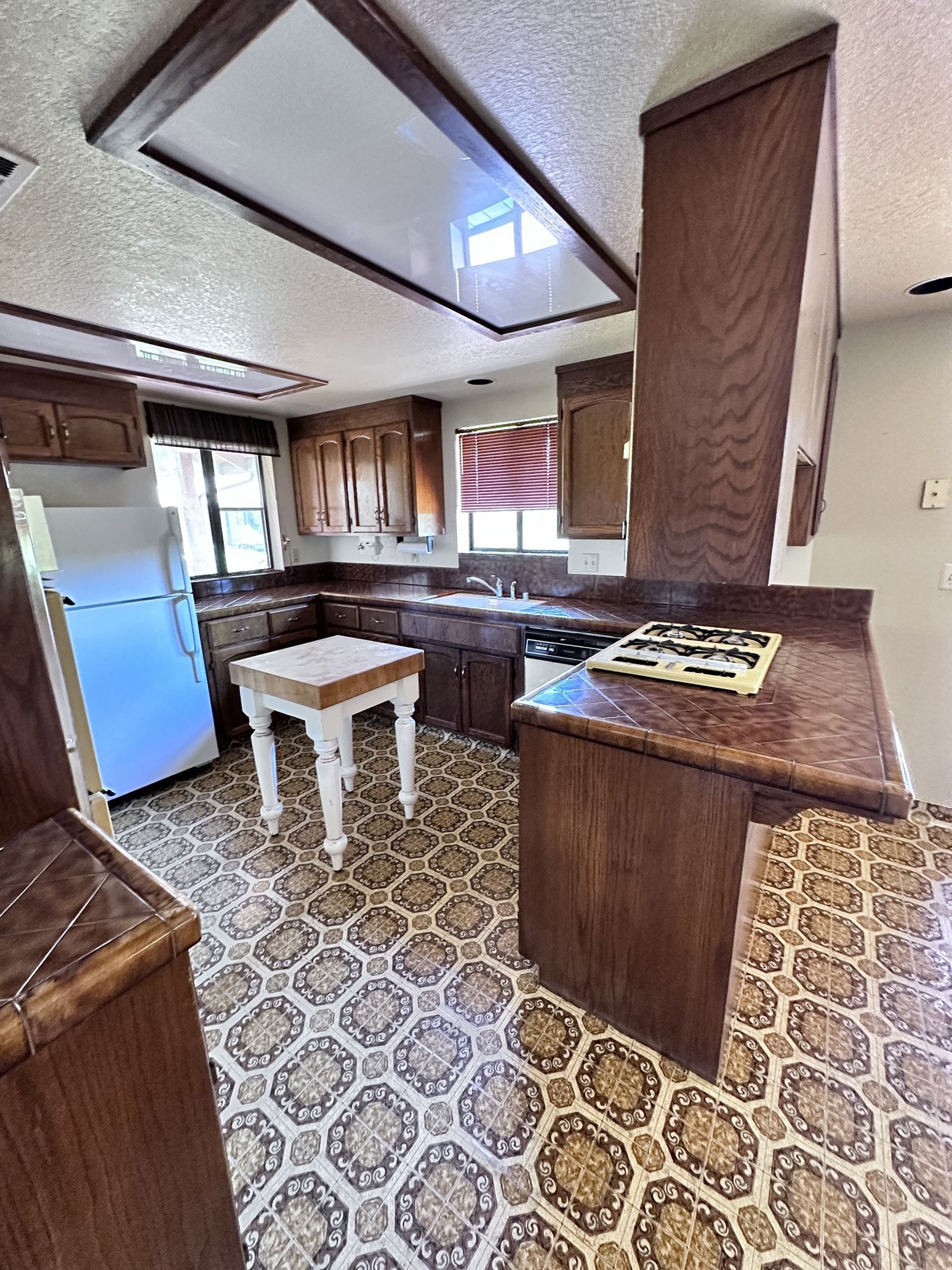 Kitchen before remodel with wood cabinets, tile countertops, older appliances, and patterned flooring