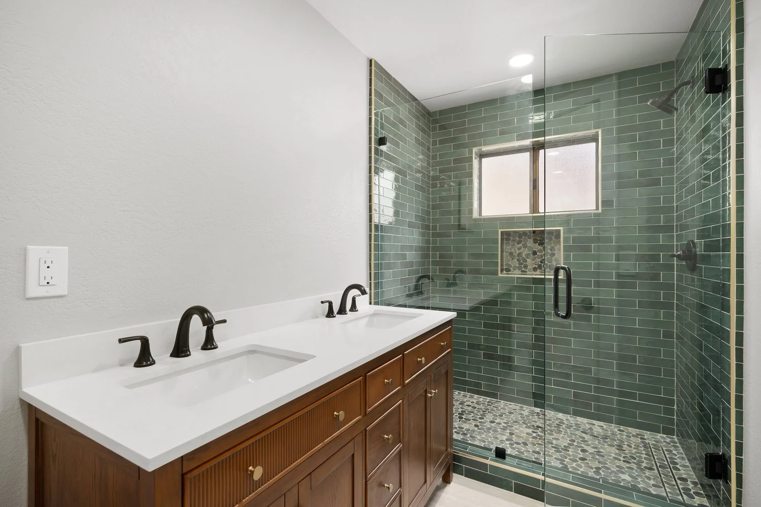 Completed bathroom remodel with double vanity, glass walk-in shower, green tile, and pebble shower floor