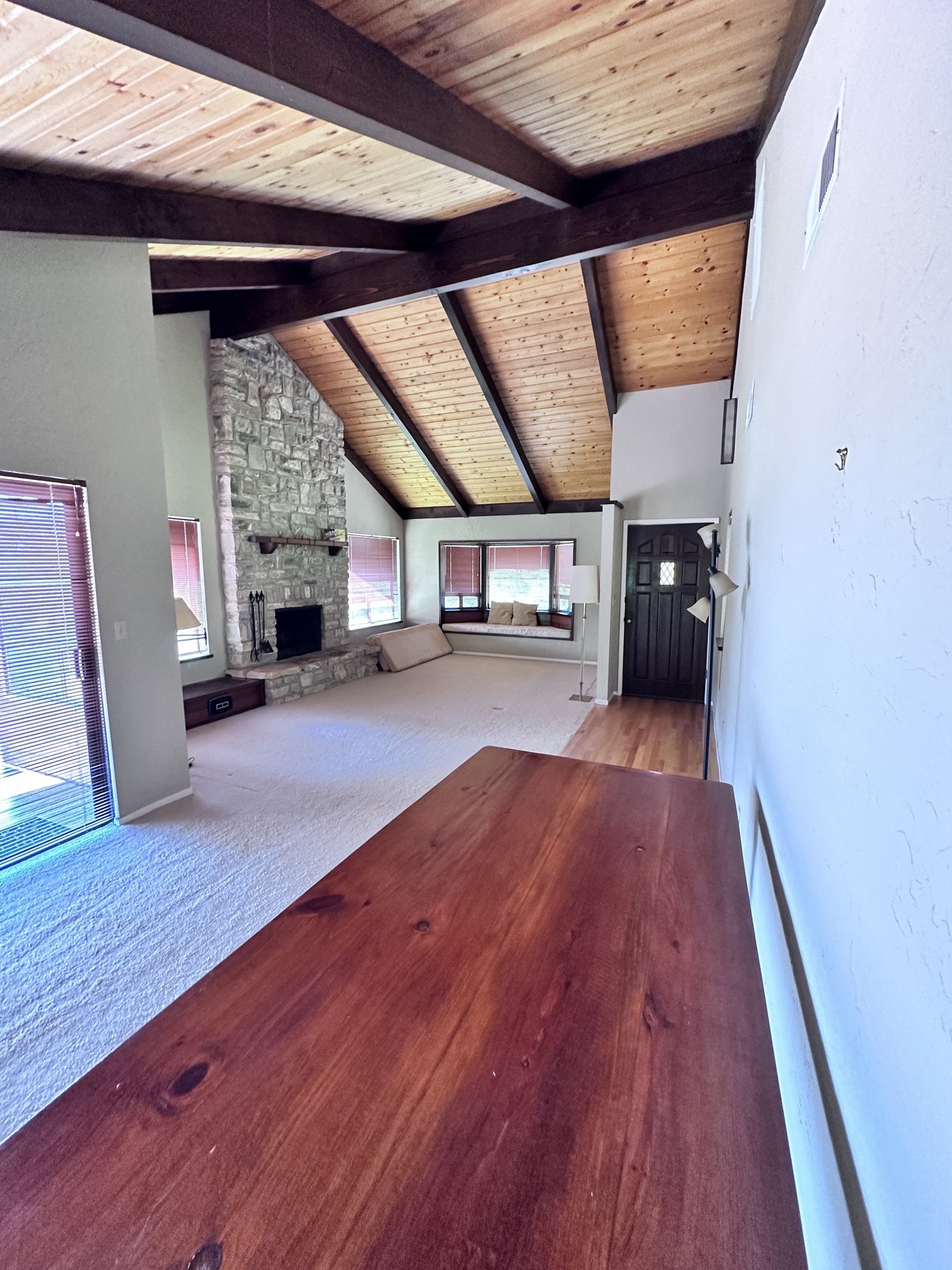 Living room before remodel with vaulted wood ceiling, stone fireplace, carpet, and dark window coverings