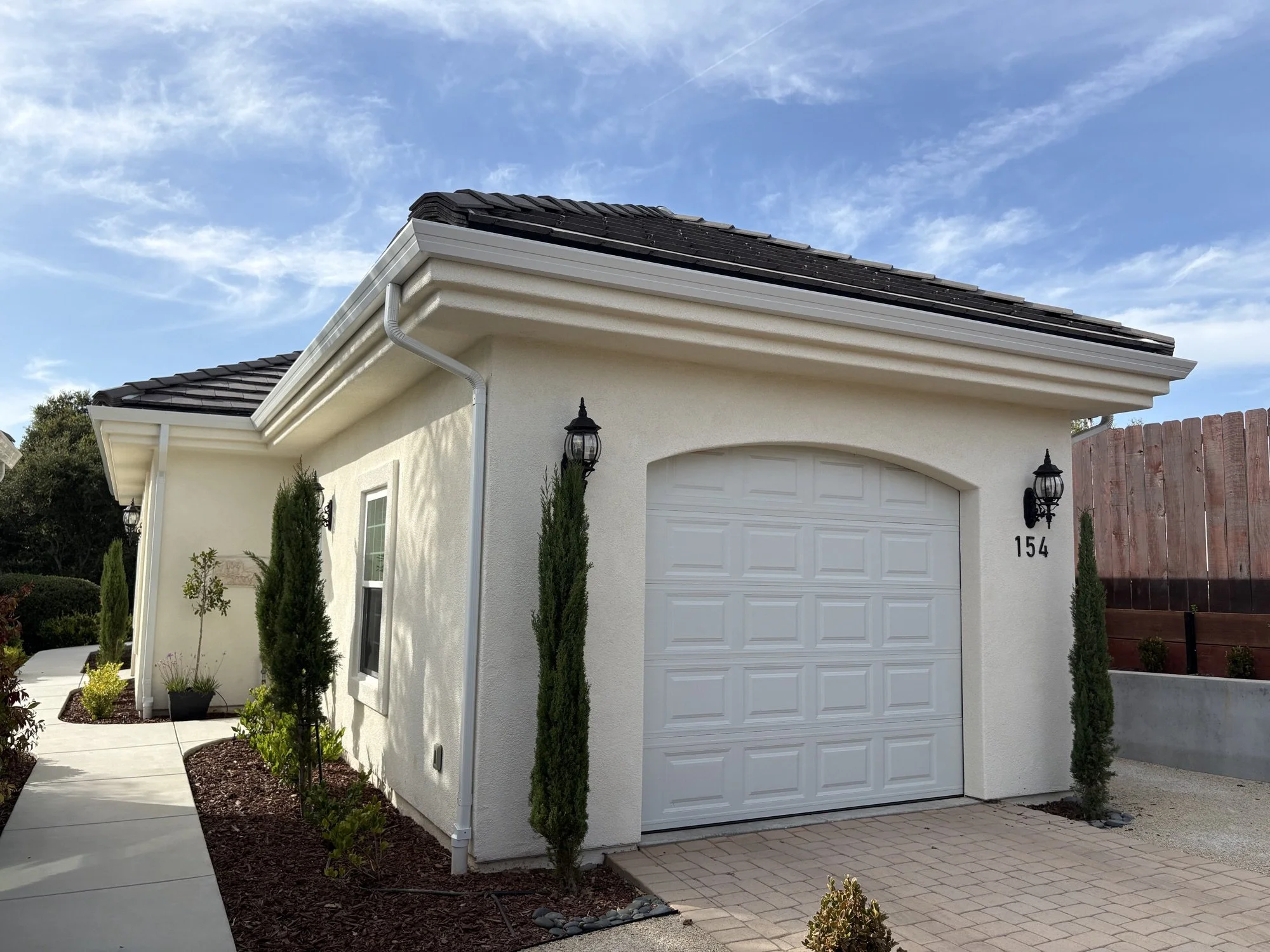 Finished garage exterior with stucco walls, white garage door, tile roof, and updated landscaping