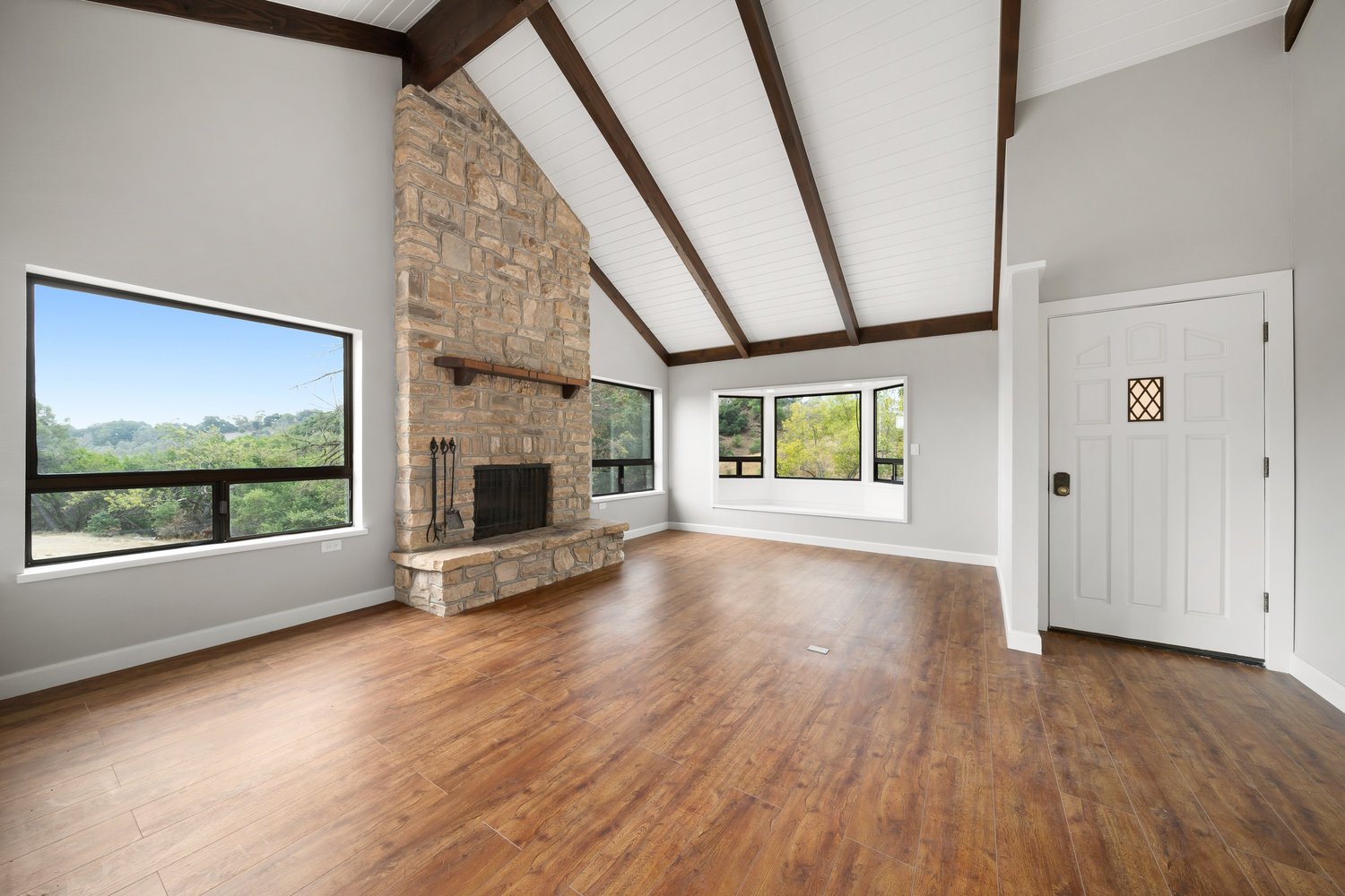 Finished living room remodel with vaulted ceiling, stone fireplace, wood flooring, and large picture windows