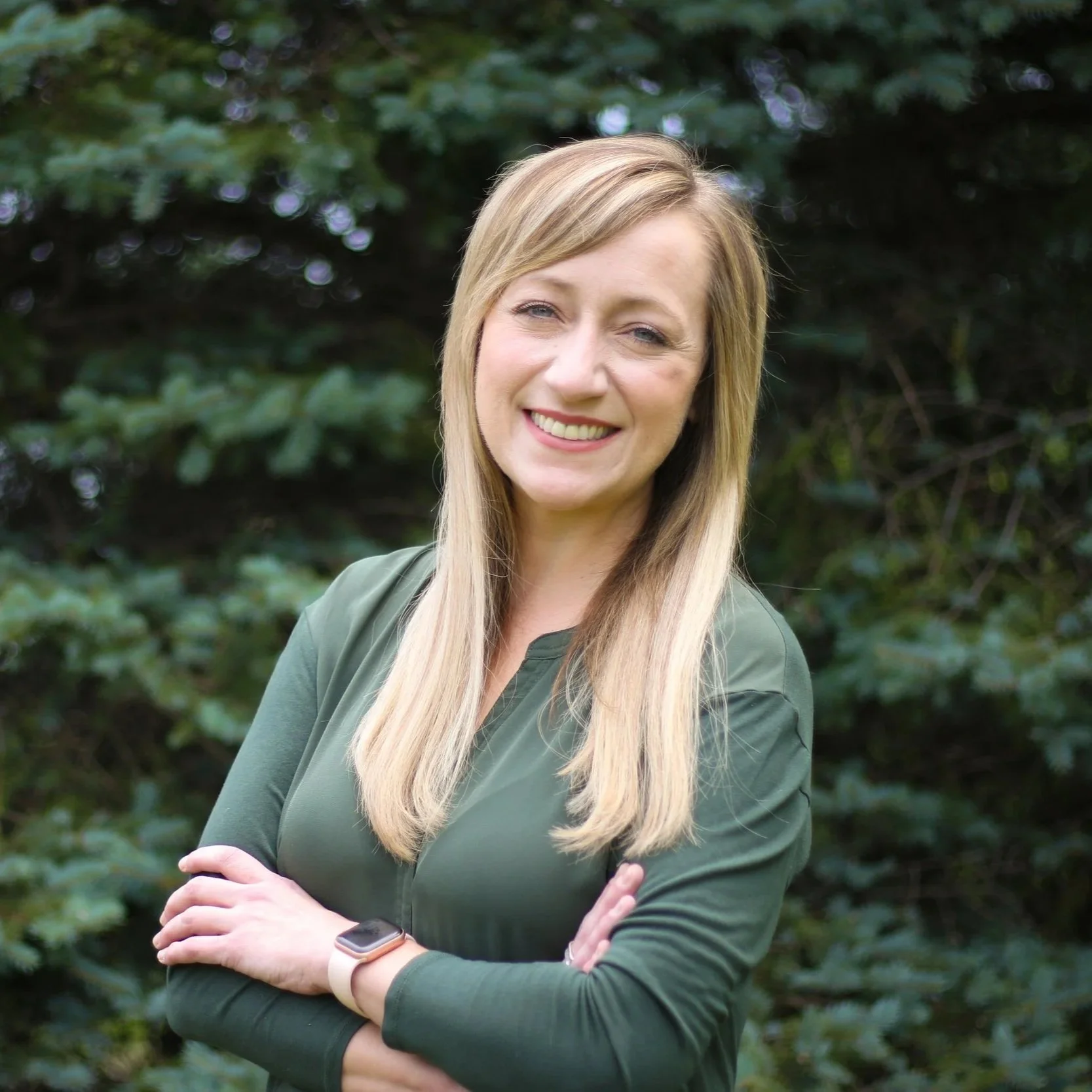 A smiling woman with long, wavy blonde hair wearing large black glasses and a black blazer with a white shirt underneath.