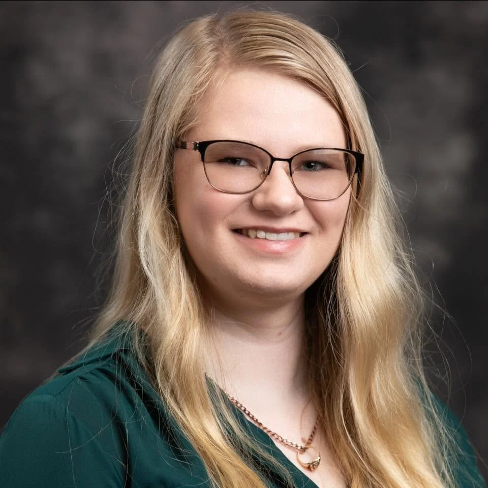 Youngg woman smiling with long blonde hair and glasses wearing a green top