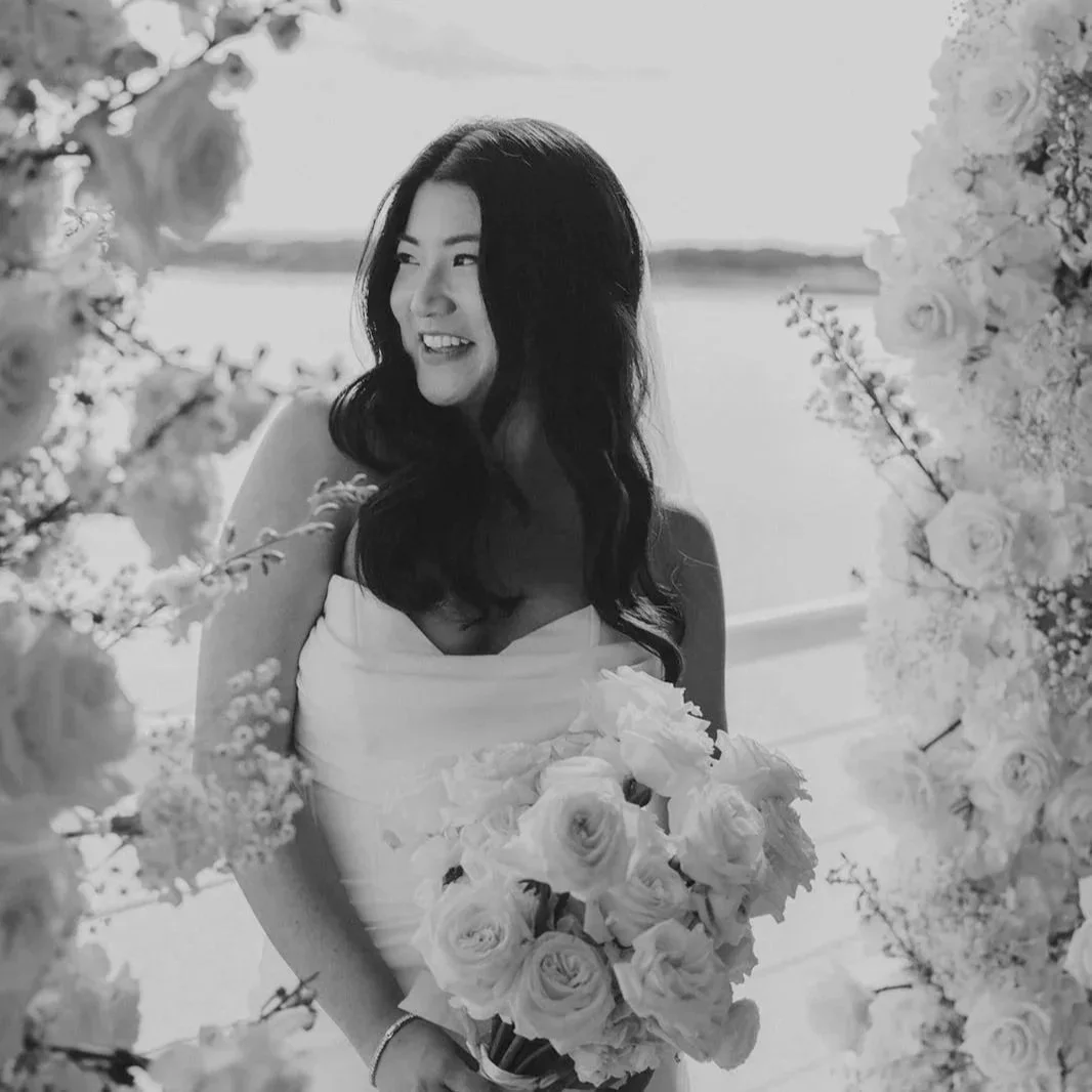 A young woman in a lace dress holding a bouquet of flowers, smiling outdoors.