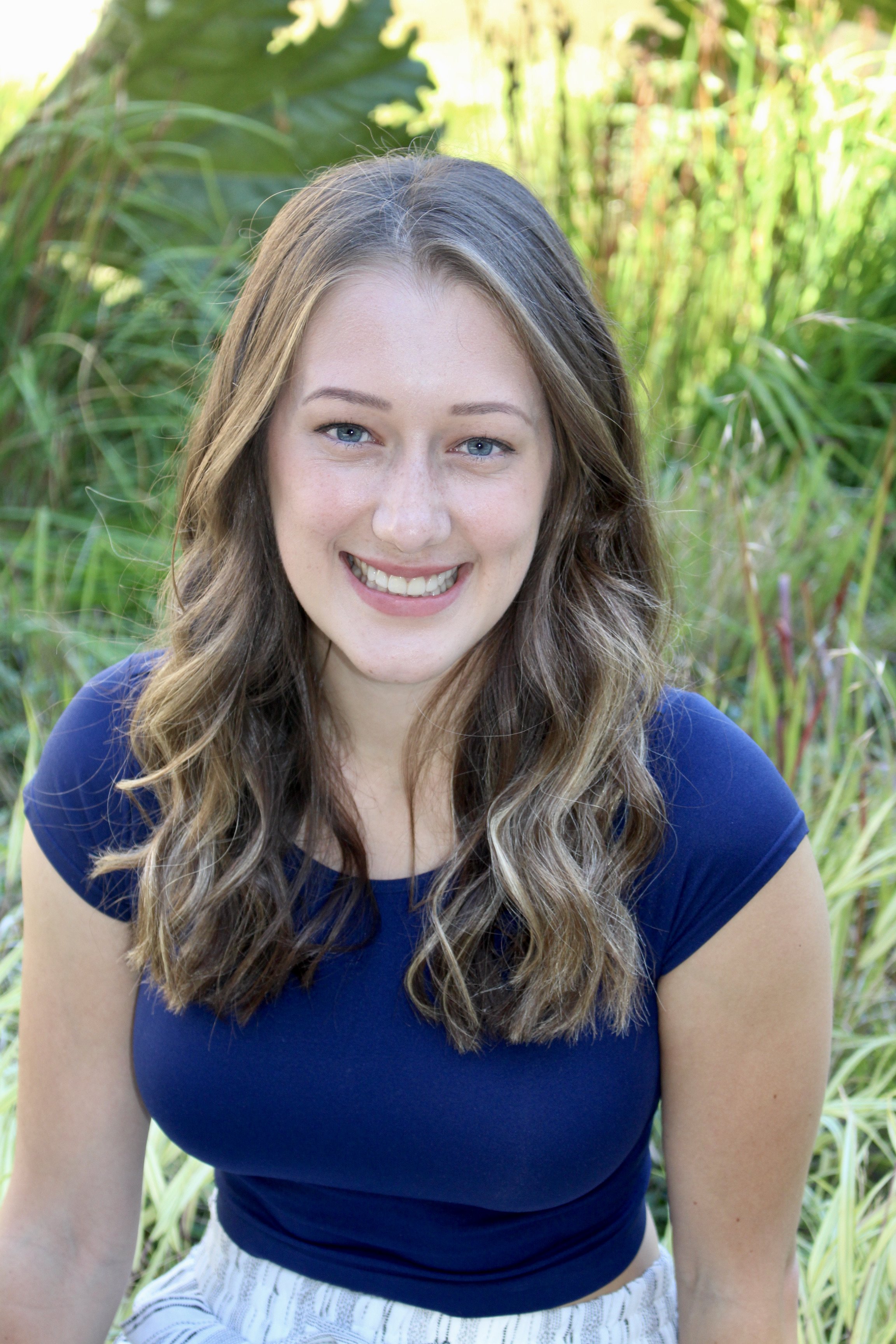 Image of a smiling woman in a blue shirt surrounded by nature