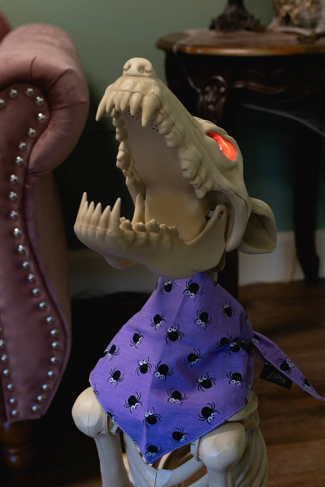 A dog skeleton prop with glowing red eyes wearing a Halloween bandana with the text 'Trick for Treat.'