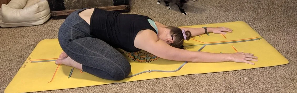 Janae doing yoga at home on her yellow mat with her cats in childs pose