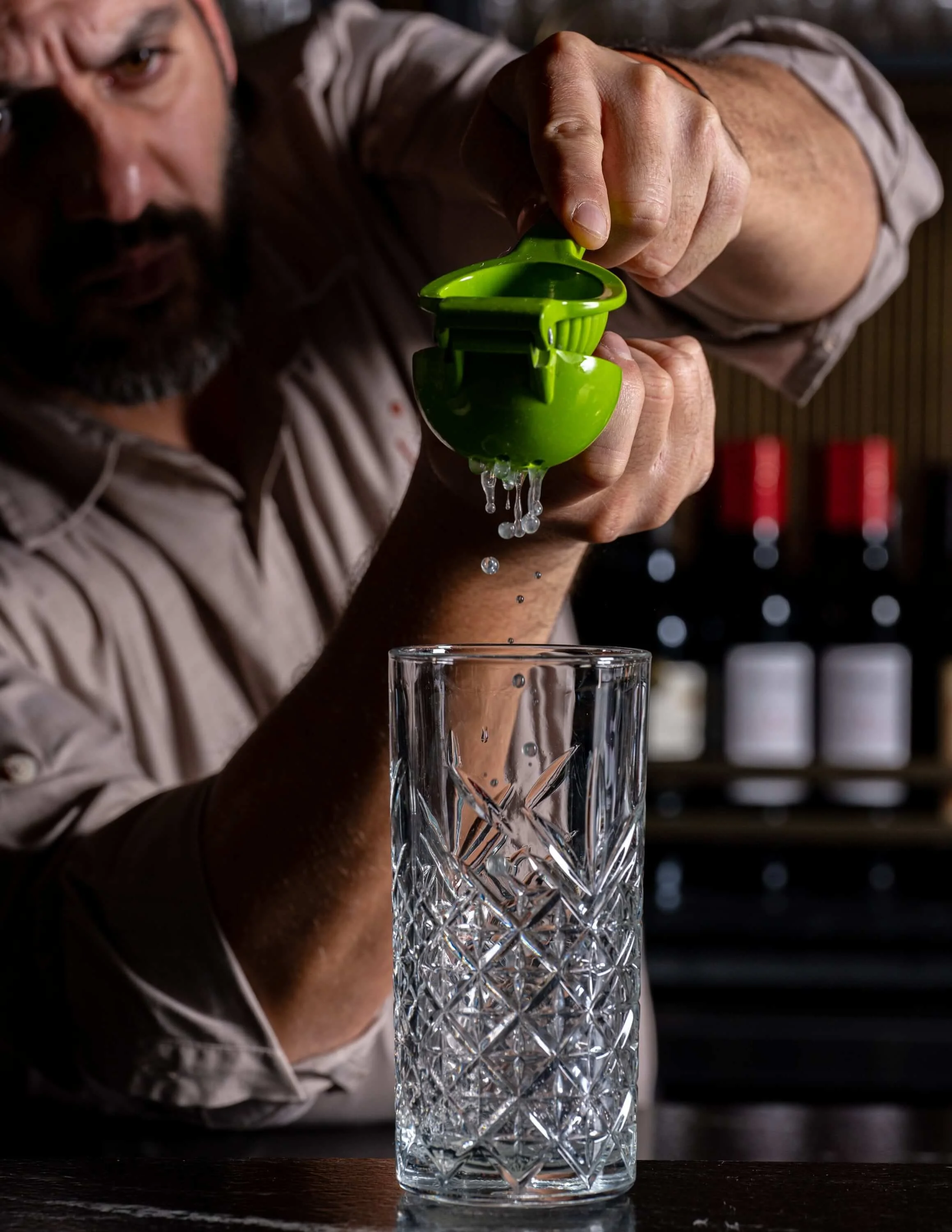  A man squeezing fresh lime juice into a tall cocktail glass 