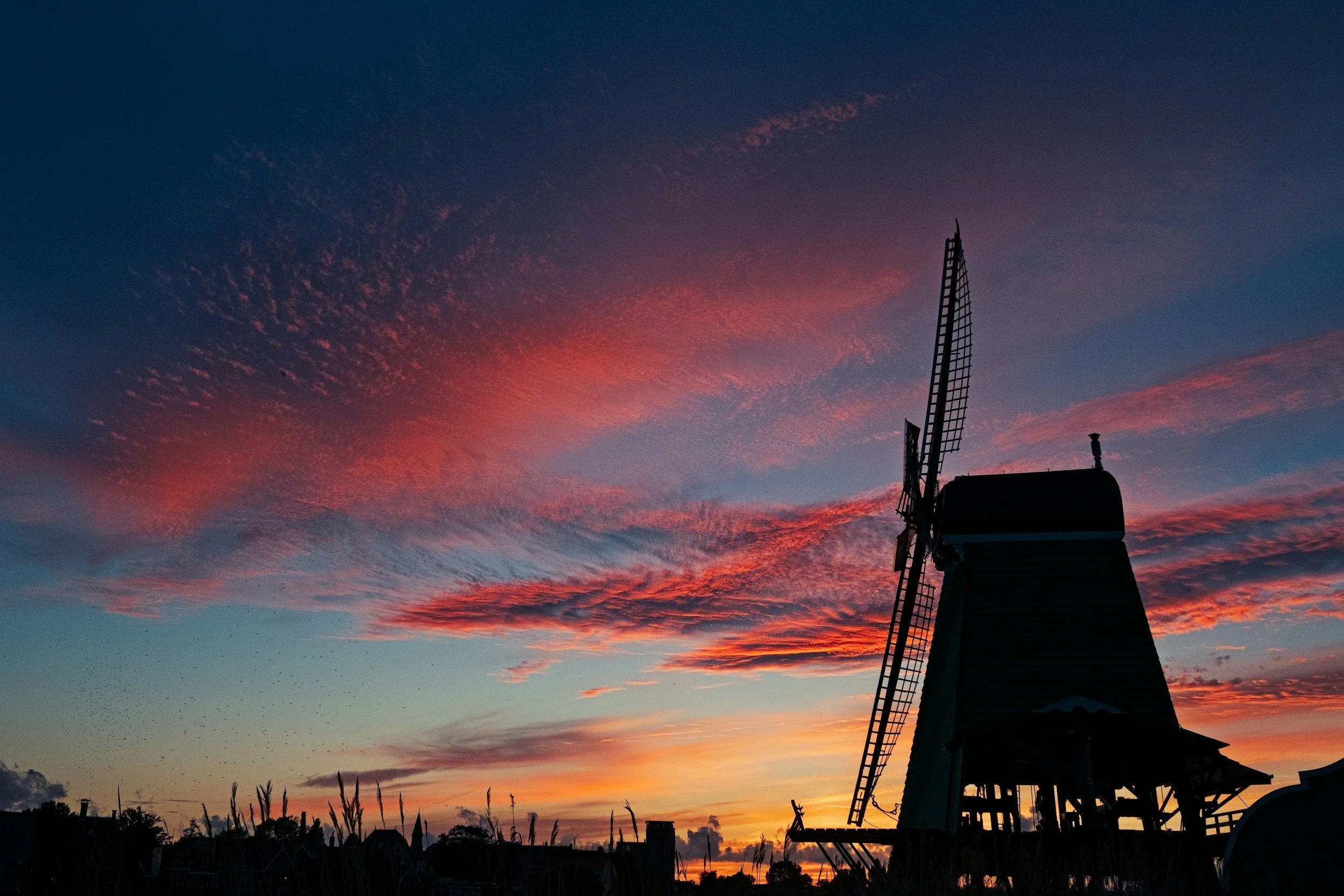 Silhouette of a traditional windmill at sunset with pink and purple clouds in the sky.
