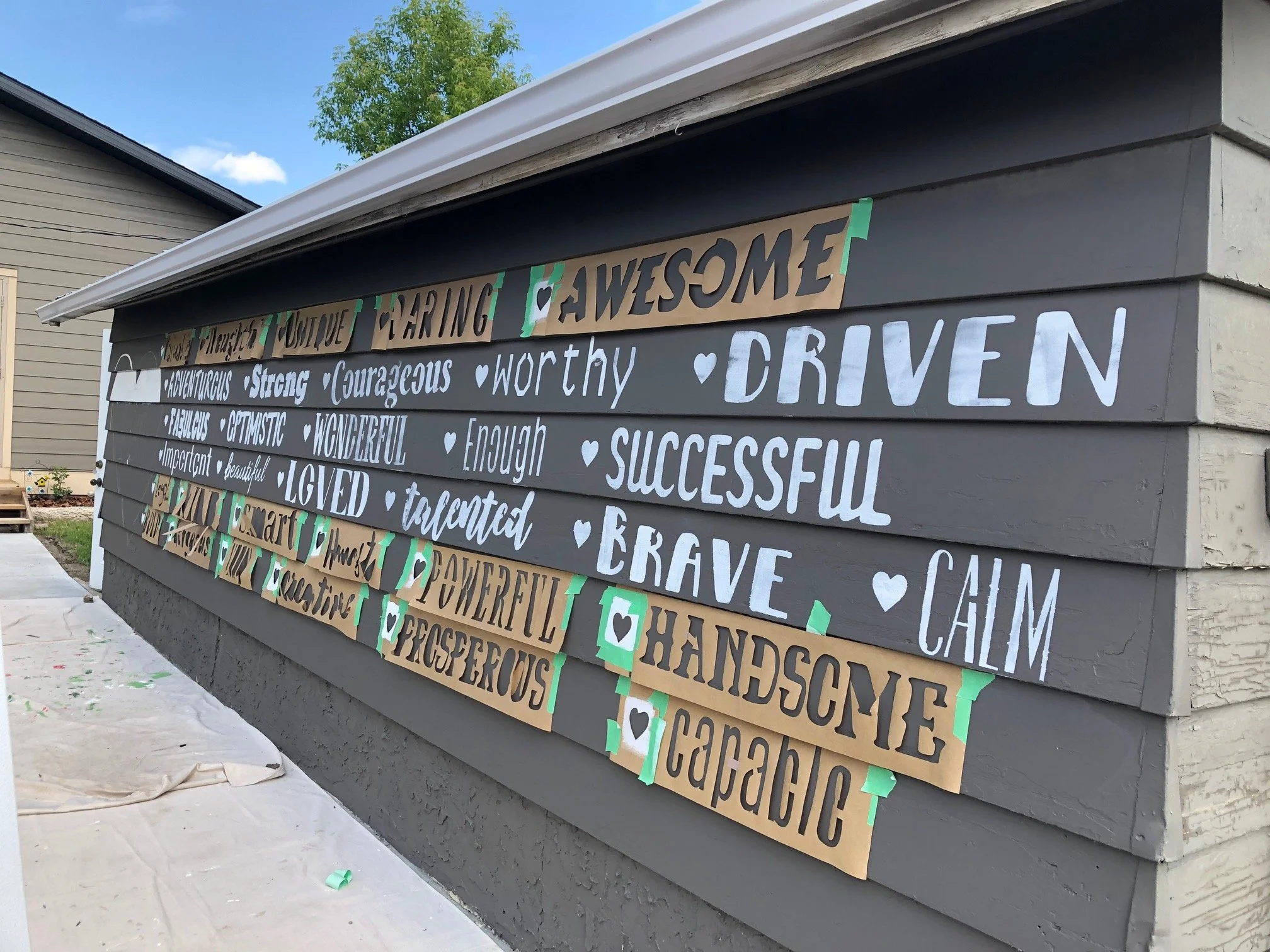 Word templates taped on the Blessingways Family Wellness garage doors in Airdrie, Alberta, during the early stage of the Affirmation Wall mural as primer is applied before painting.